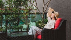 A person sitting on a wicker chair with a red cushion, surrounded by greenery and a glass table. - Royal Rose Hotel Xinsheng (Taipei)