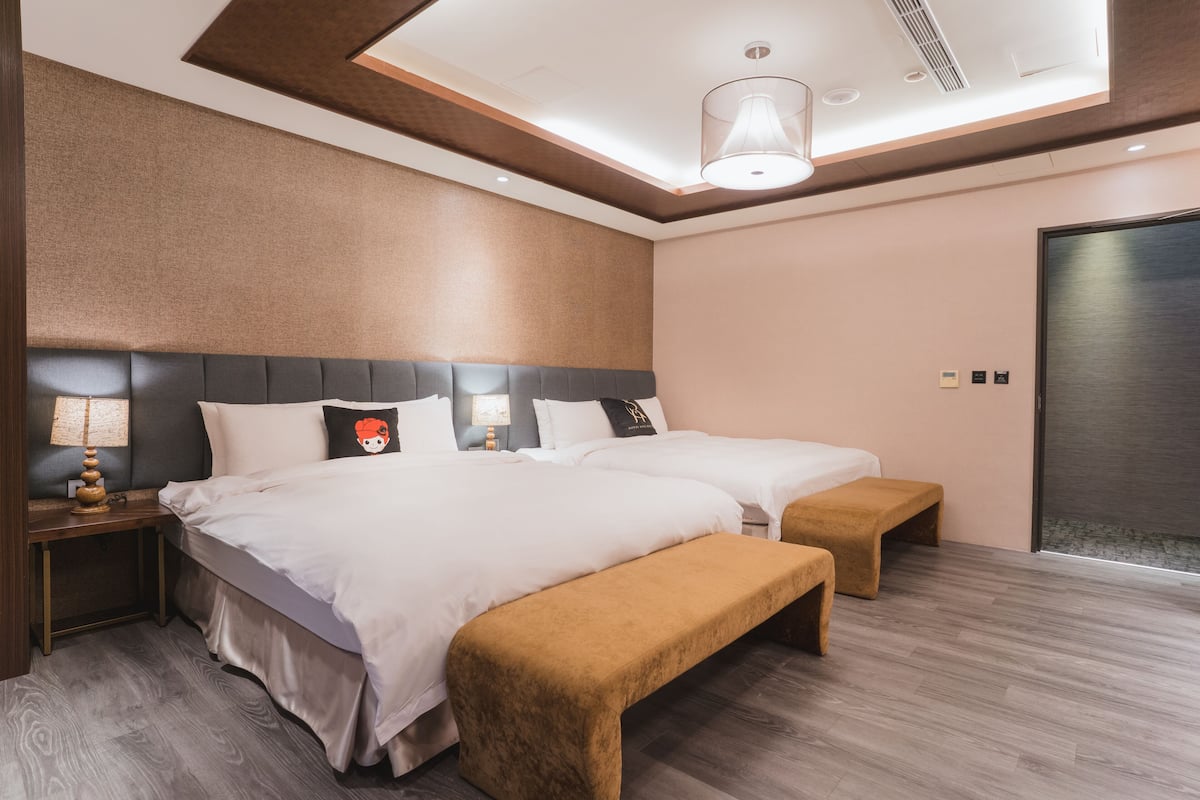 Una habitación de hotel moderna con dos camas, un banco, una mesita de noche y una lámpara en el techo.
