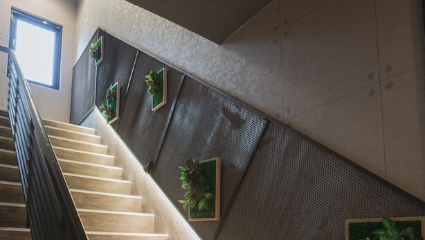A staircase with wooden steps and a metal handrail, leading to a landing with a textured wall and green plants. - Royal Rose Hotel Xinsheng (Taipei)