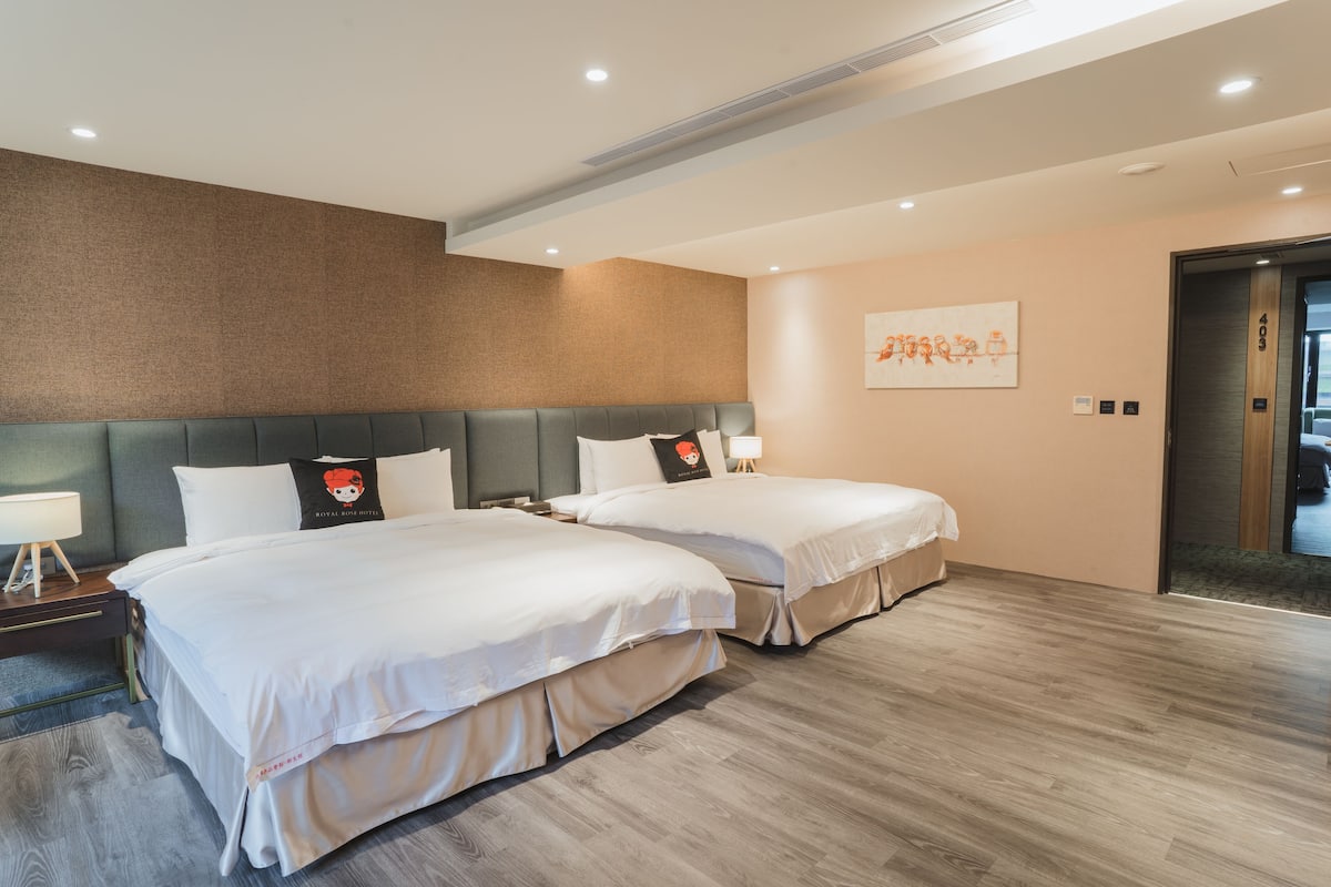 Habitación de hotel con dos camas, cabecero gris, suelo de madera y un cuadro en la pared.