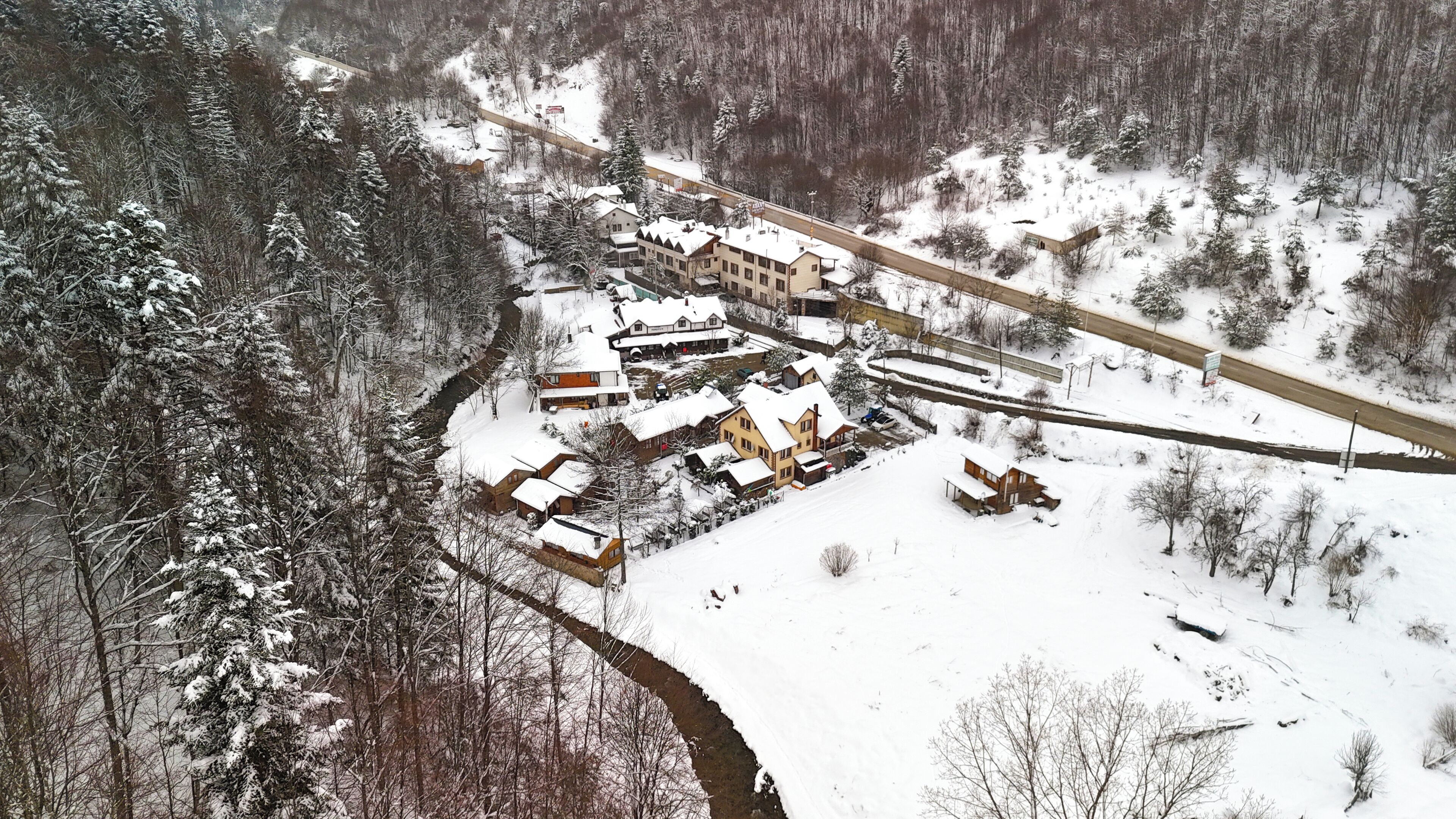 Un pueblo cubierto de nieve con una mezcla de edificios residenciales y comerciales, una carretera y un puente.