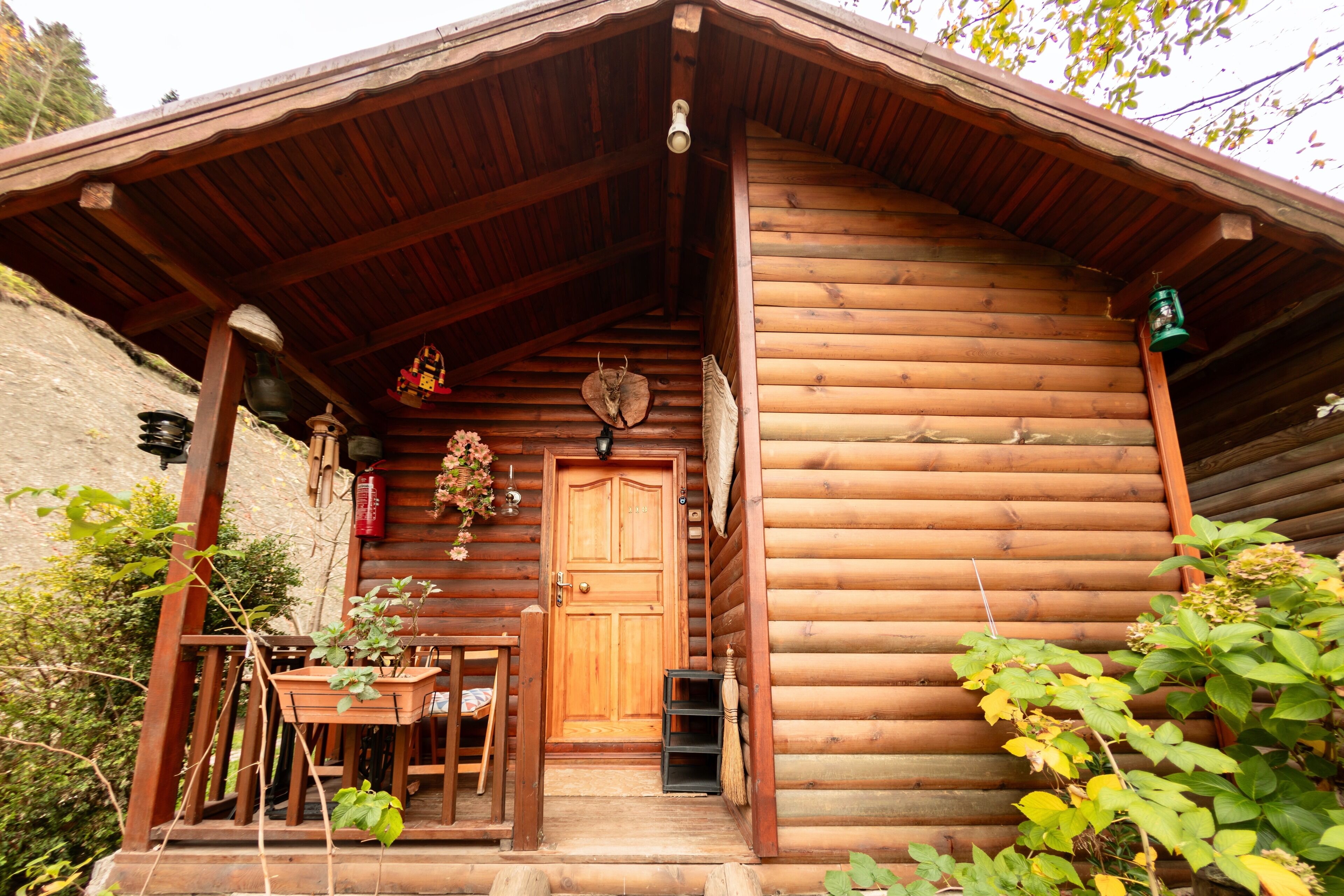 A wooden log cabin with a wooden door, a small porch with a table and chairs, and a lantern hanging on the porch.