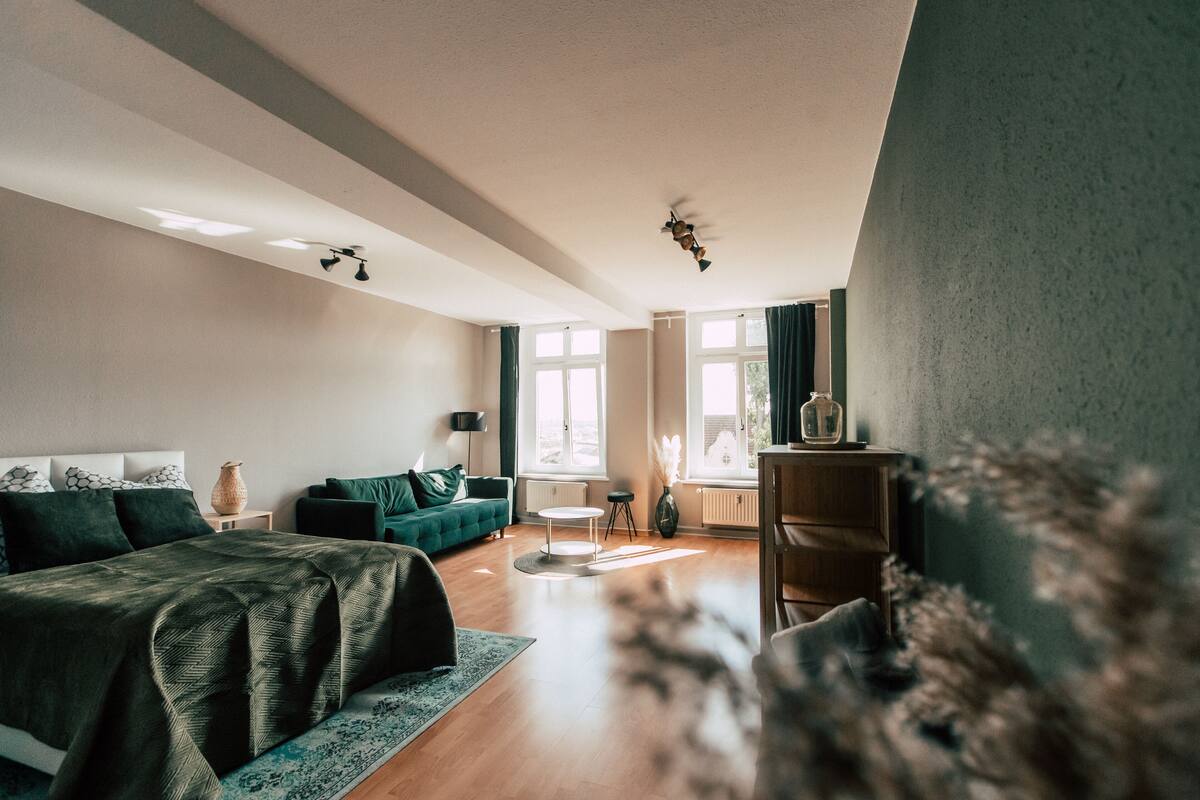 A modern bedroom with a bed, a green sofa, a small table, and a window with curtains.
