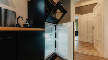 Une cuisine compacte dotée d’un réfrigérateur et d’un four encastrés, d’un plan de travail en bois et donnant sur une pièce adjacente.