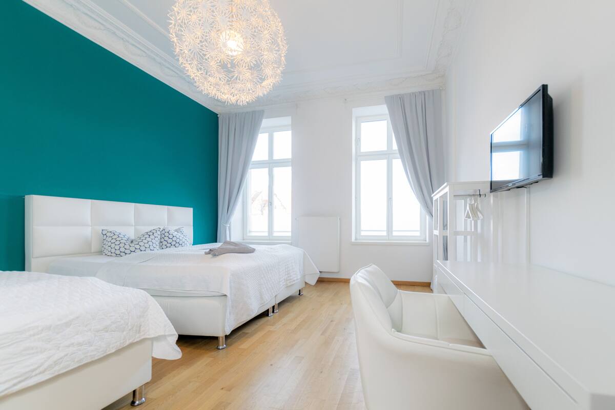 A modern bedroom with two beds, a TV, and a chandelier.