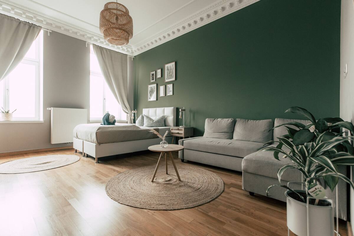 A modern living room with a green accent wall, a grey sofa, a round coffee table, and a large window with curtains.