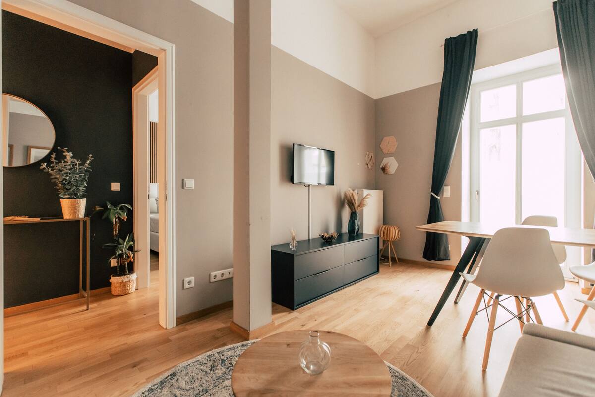 A modern living room with a wooden floor, a round coffee table, a black TV stand, and a dining area with a table and chairs.
