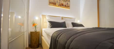A bedroom with a bed, a nightstand, a painting, and a vase with flowers.