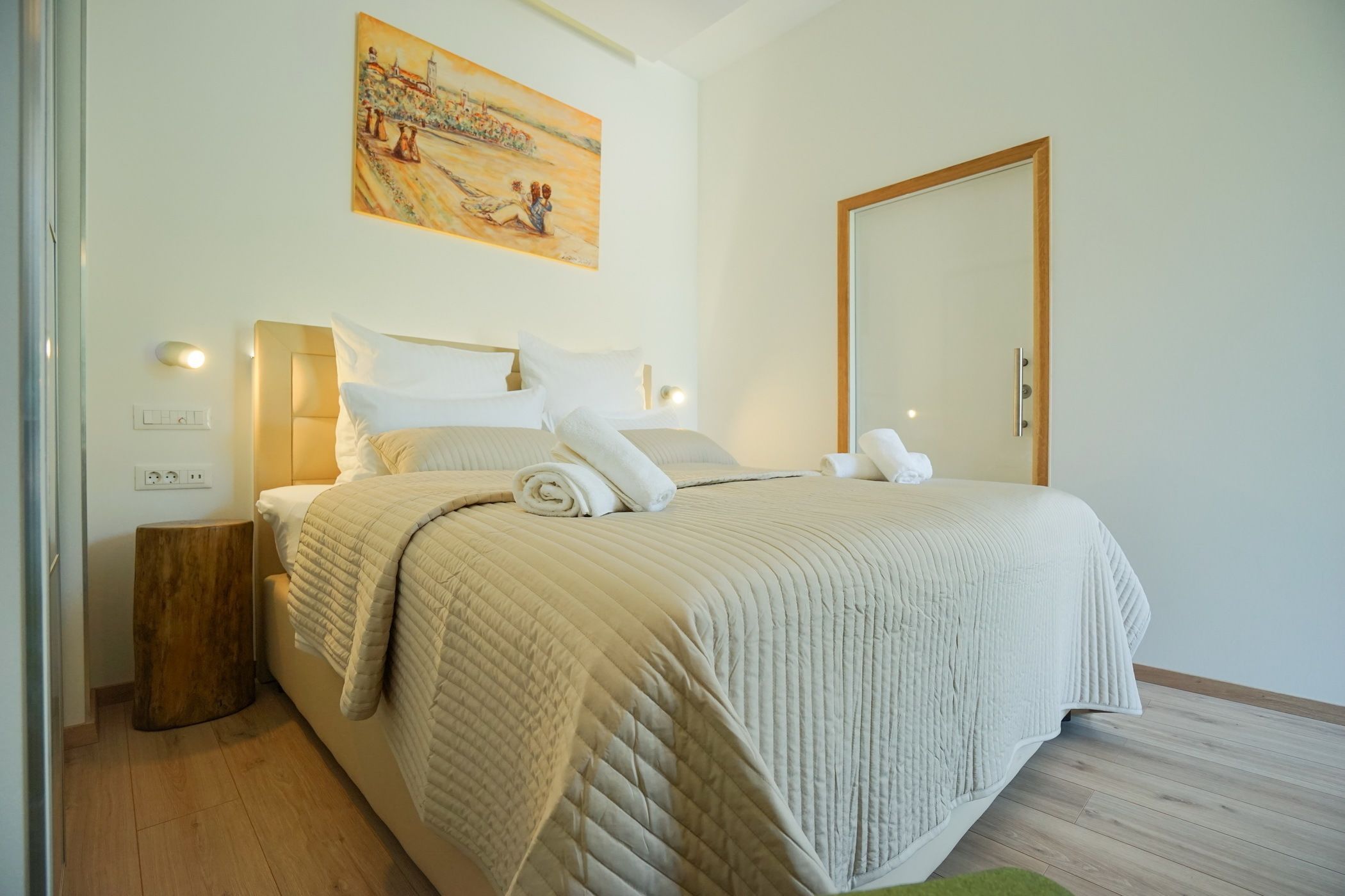 Una cama bien hecha con un edredón acolchado, una lámpara de noche y una mesita de noche de madera.