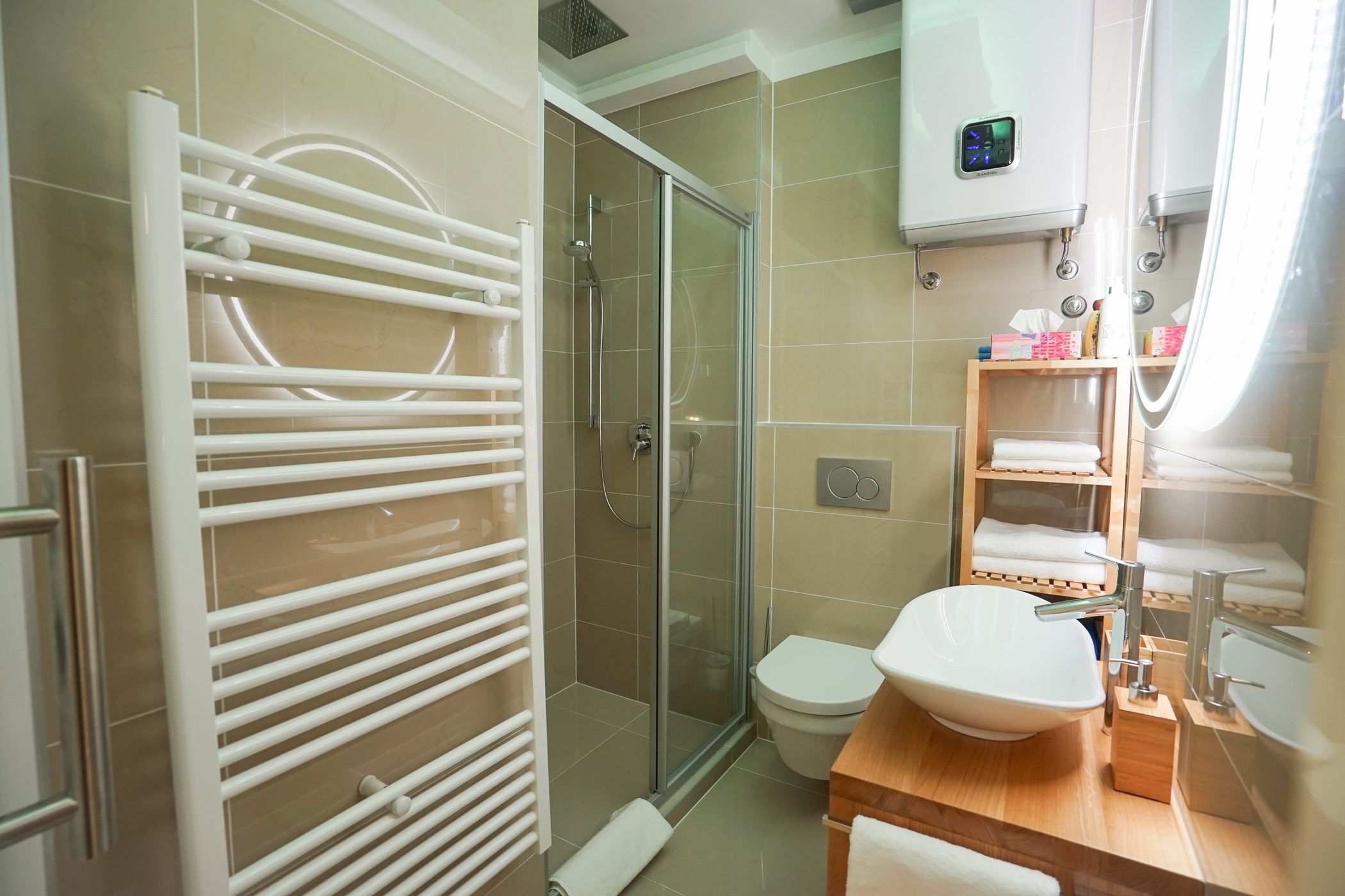 A bathroom with a glass shower enclosure, a white toilet, a sink with a wooden countertop, and a towel rack.