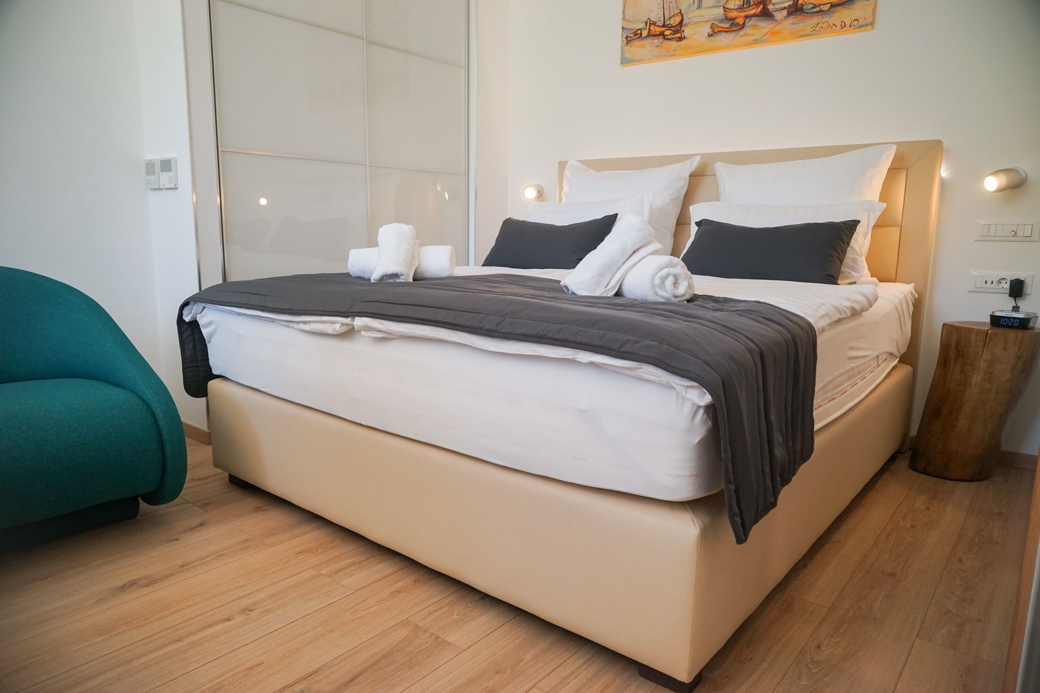 A modern bedroom with a large bed, a teal chair, and a wooden floor.