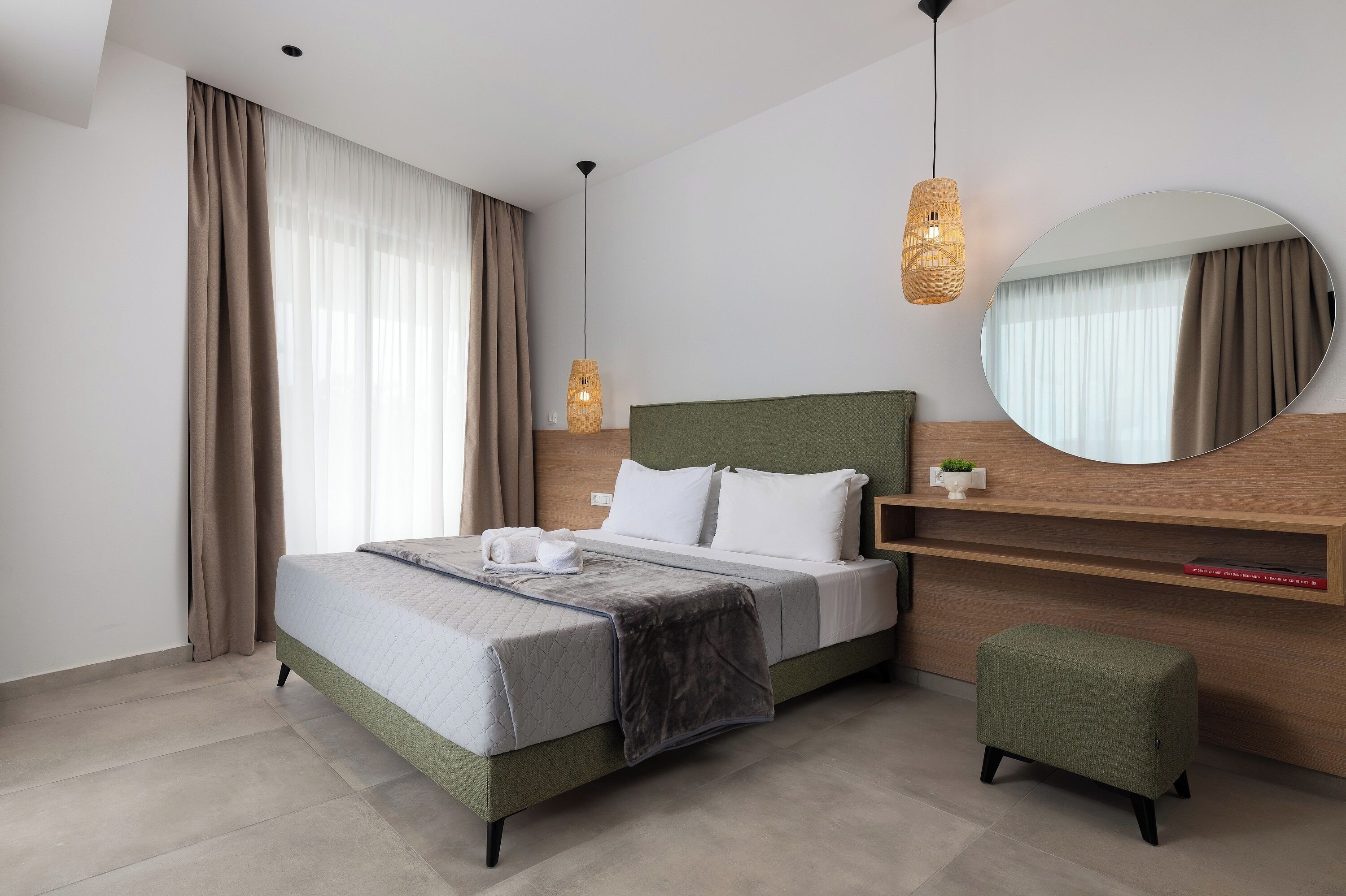 Une chambre d’hôtel moderne équipée d’un lit, d’une table de chevet, d’un miroir et d’un luminaire suspendu.