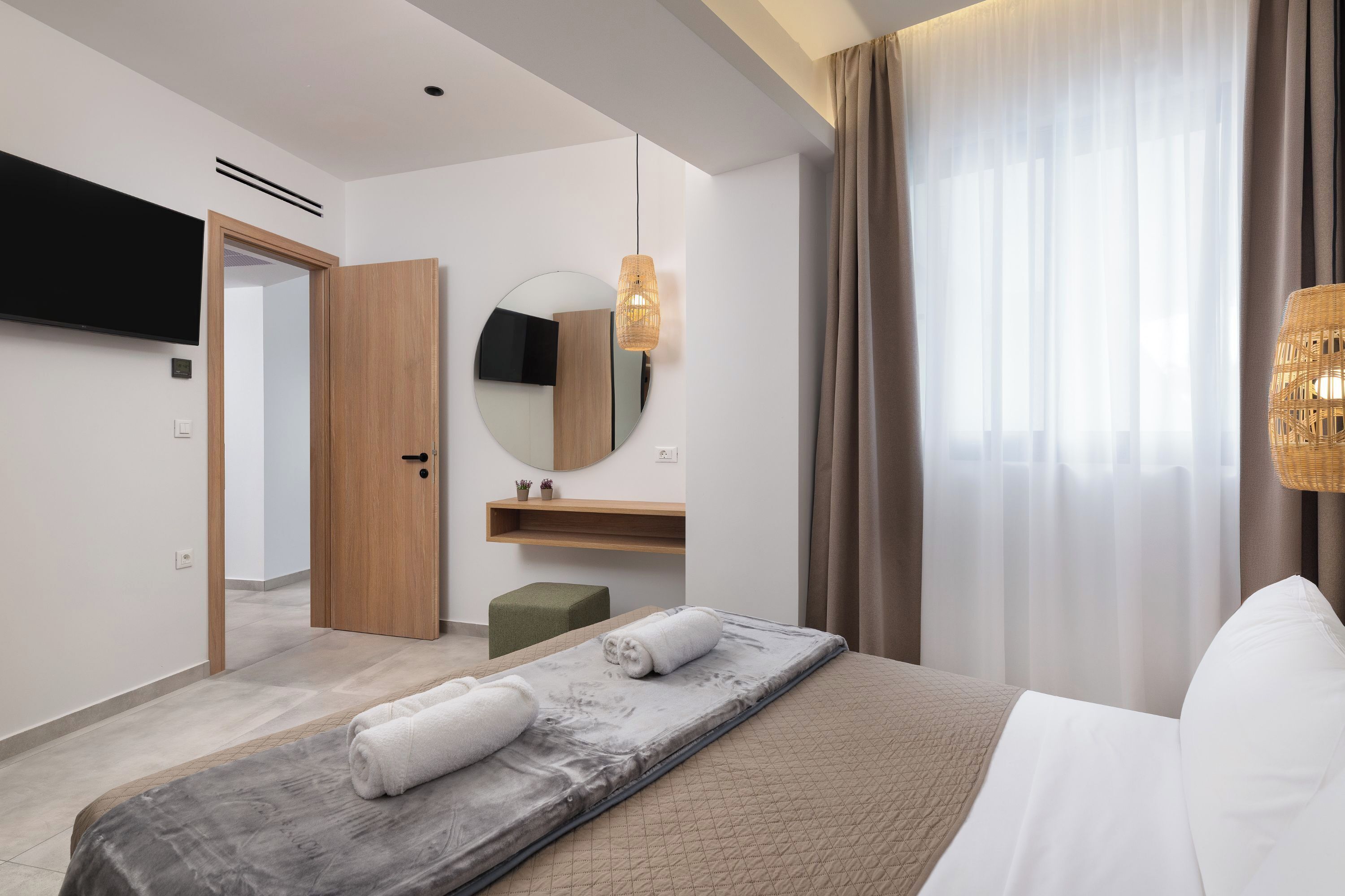 A modern hotel room with a bed, a mirror, a television, and a window with curtains.