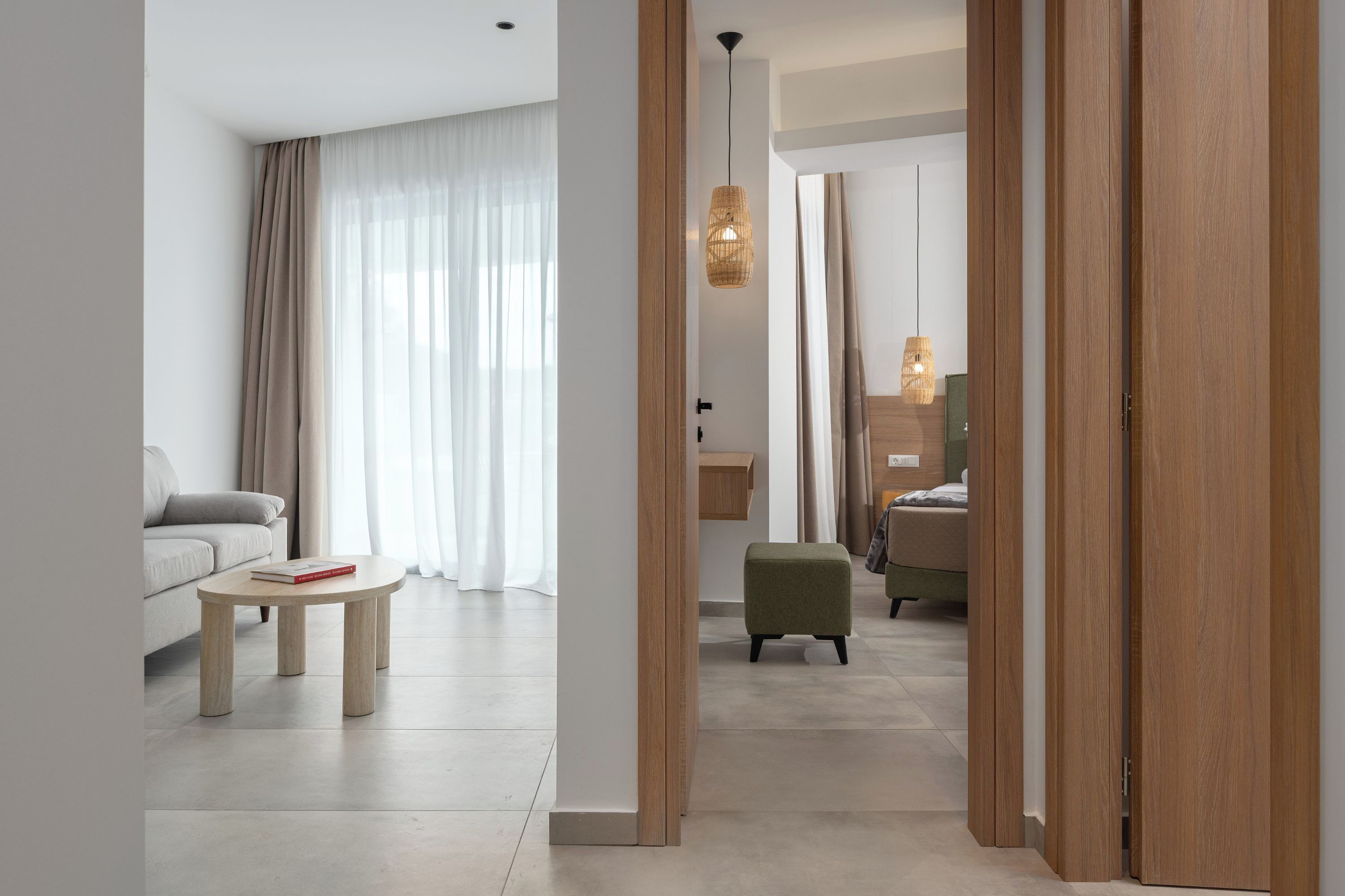 A modern hotel room with a sofa, a small table, a green ottoman, and a wooden wardrobe.