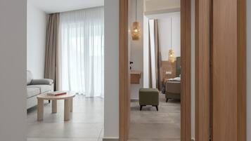 A modern hotel room with a sofa, a small table, a green ottoman, and a wooden wardrobe.