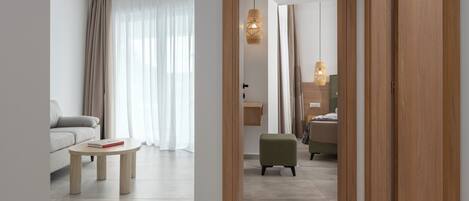 Ein modernes Hotelzimmer mit einer Couch, einem kleinen Tisch, einem grünen Hocker und einem Holzschrank.