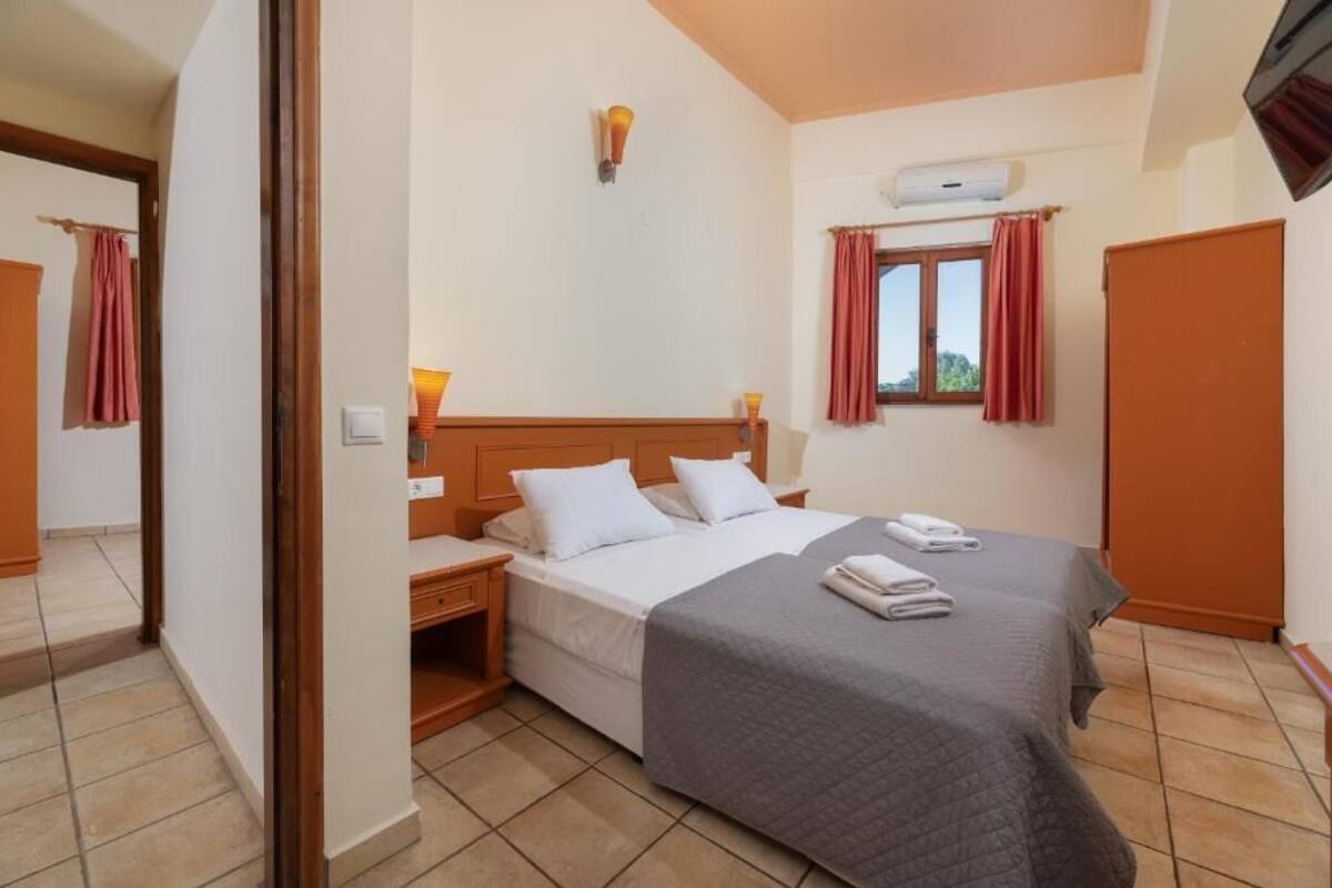 A hotel room with a bed, bedside tables, a wall-mounted air conditioner, and a window with curtains.