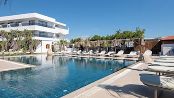 A swimming pool with lounge chairs, a modern building, and palm trees.
