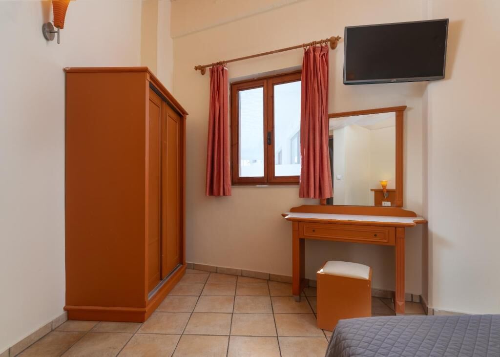 A bedroom with a bed, a wooden wardrobe, a desk with a mirror, and a window with curtains.