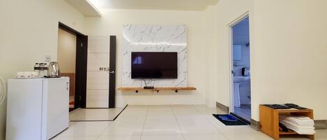 A modern living room with a flat-screen TV mounted on a marble wall, a white refrigerator, and a wooden shelf.