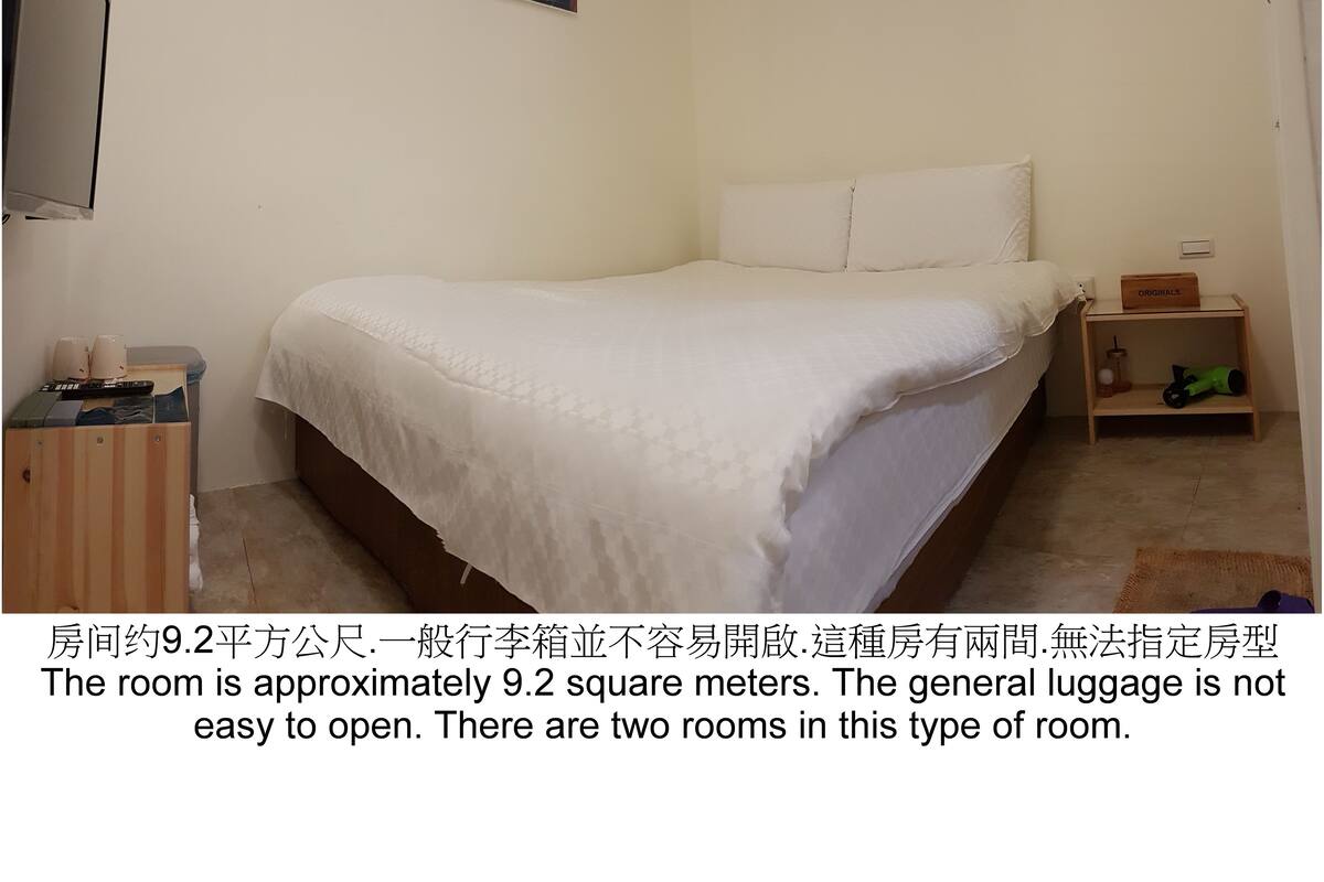 A bedroom with a bed, a nightstand, a small window, and two wall-mounted paintings.