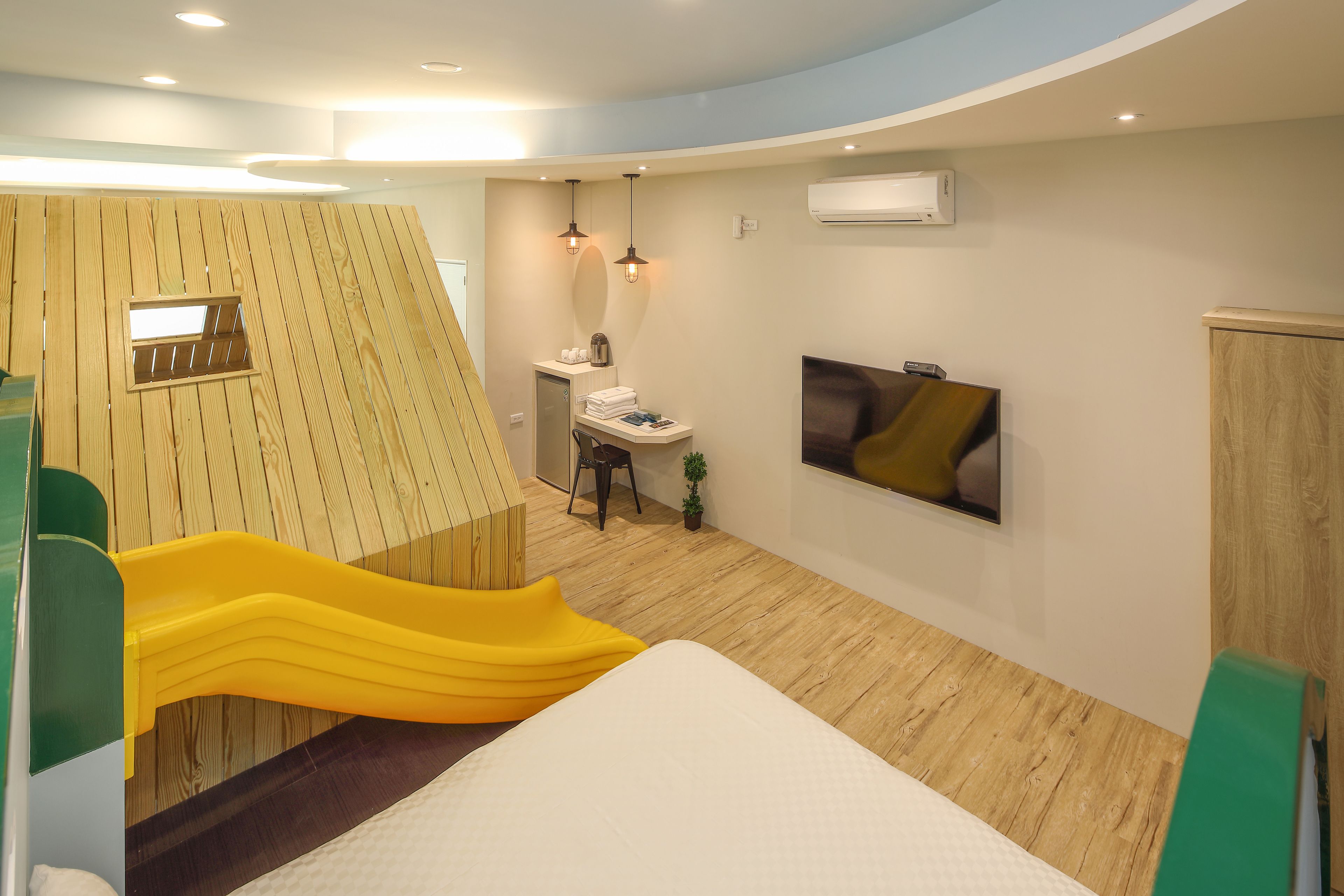 A modern room with a bed, a desk, a chair, a small table, a TV, and a window.