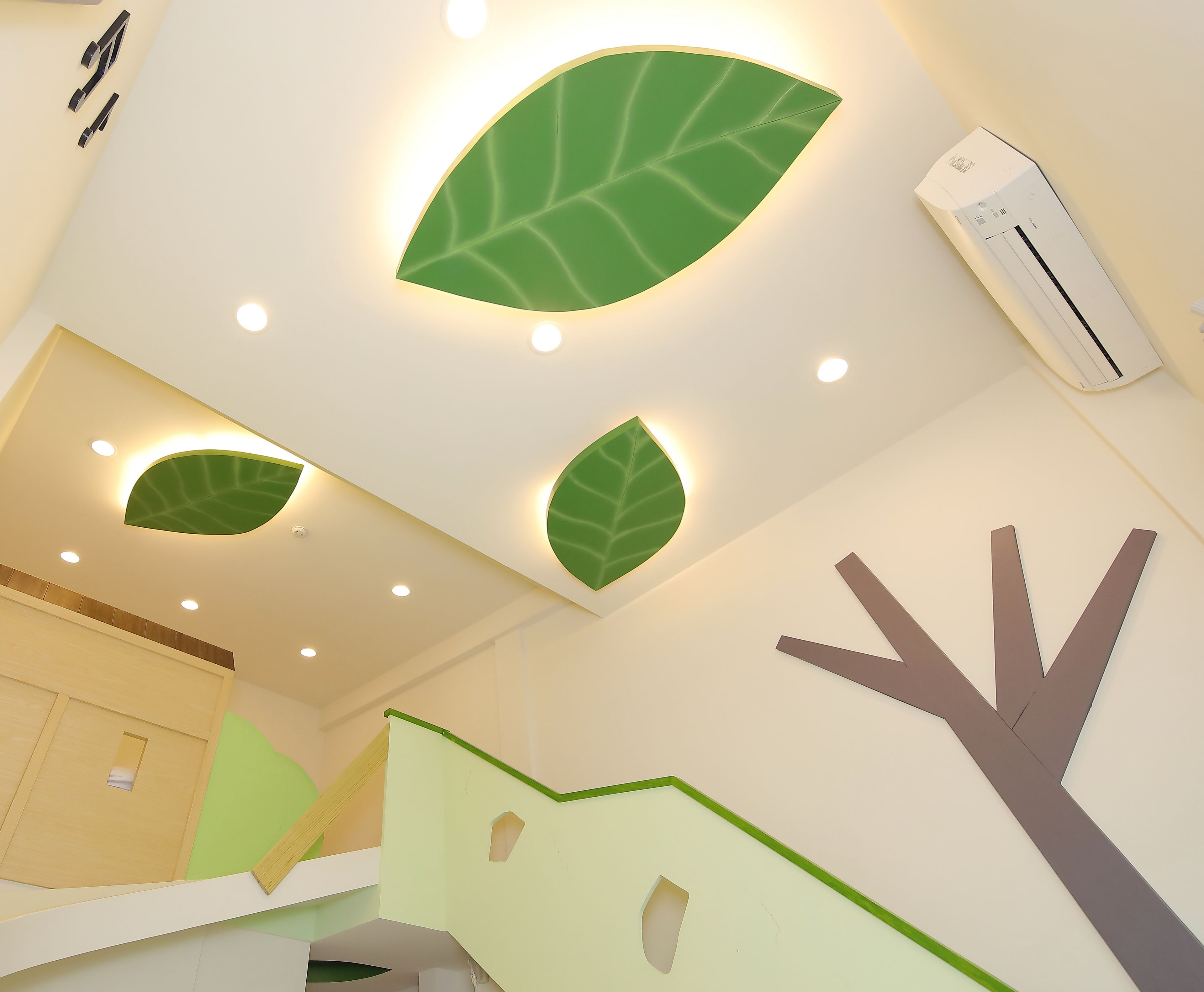 A modern room with a unique ceiling design featuring illuminated leaf shapes, a visible air conditioning unit, and a geometric wall decoration.