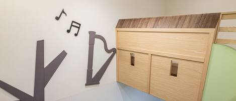 A room with a bed, a wooden cabinet, and a wall with a musical note and a harp symbol.