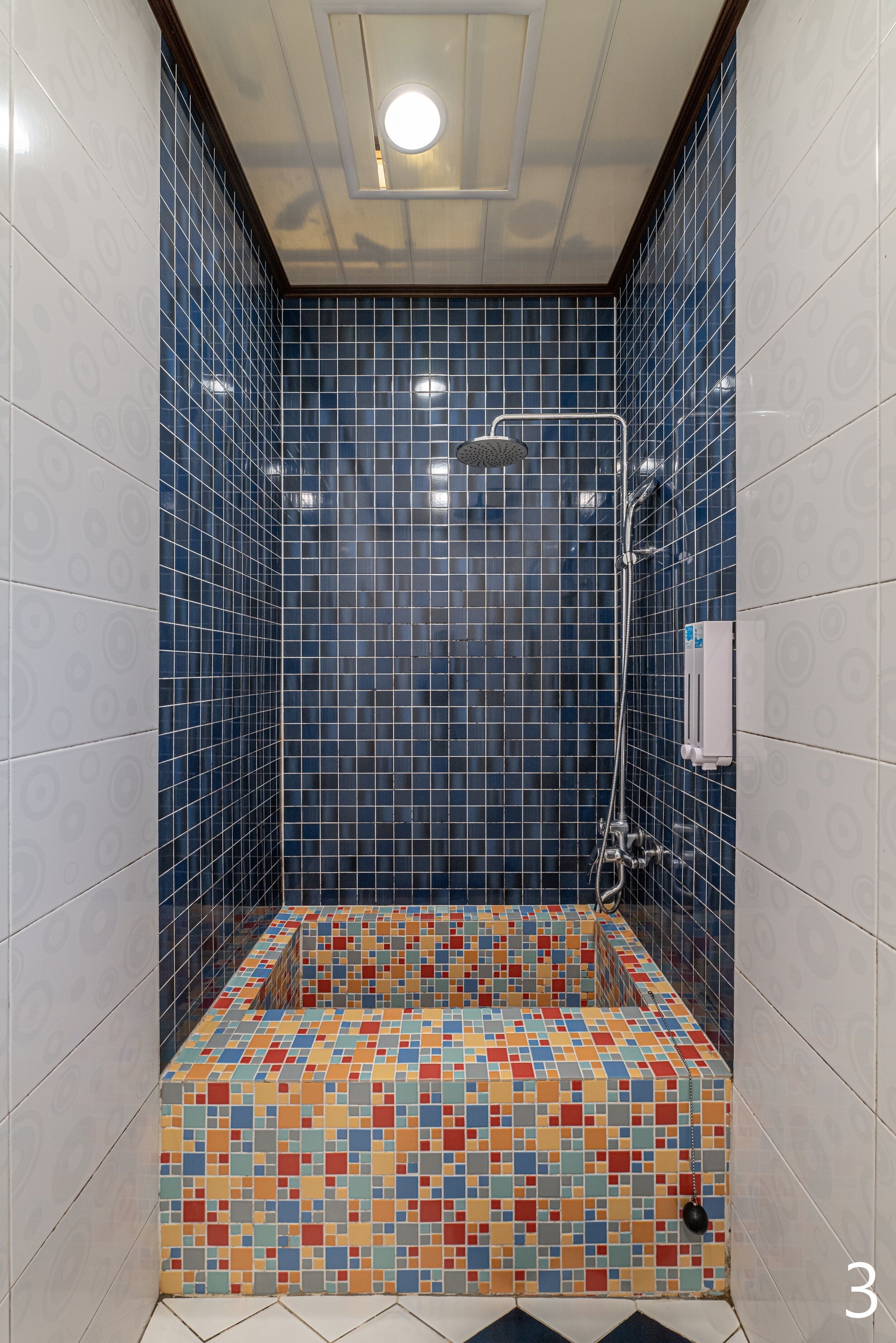 A small, tiled shower area with a colorful floor and blue-tiled walls.