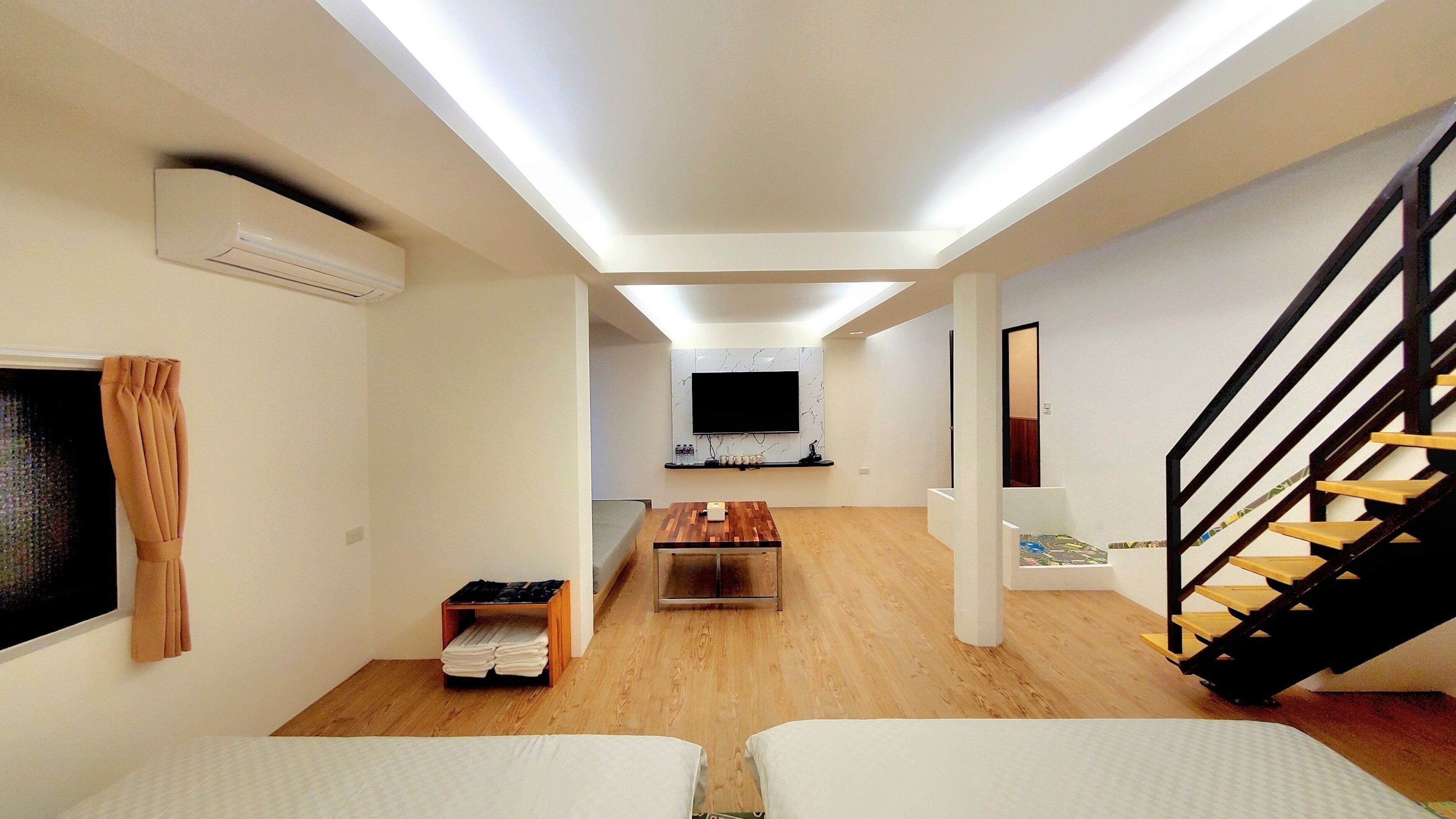 Una sala de estar moderna con una televisión de pantalla plana, piso de madera, una escalera y una pequeña mesa.