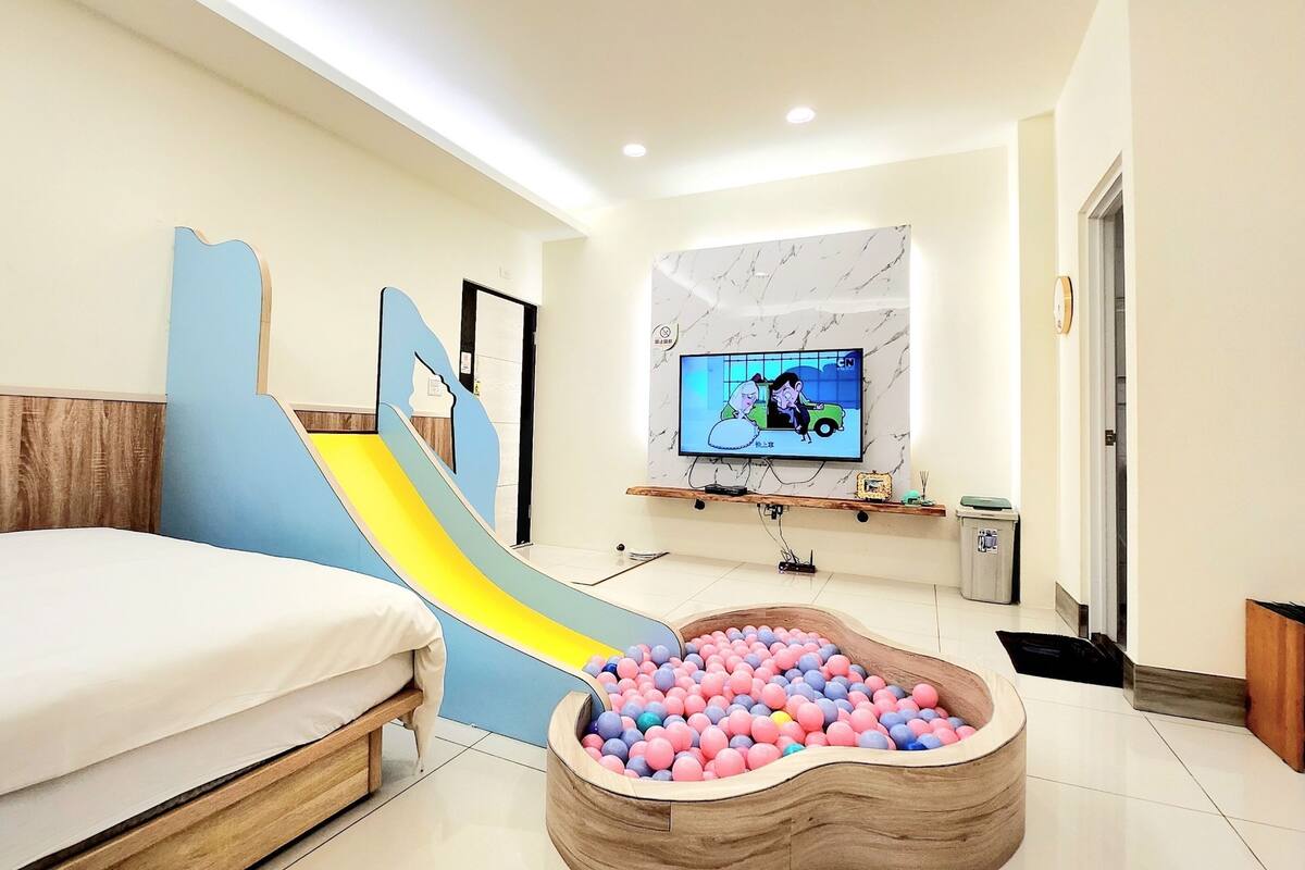 A bedroom with a bed, a TV, a marble wall, and a ball pit.