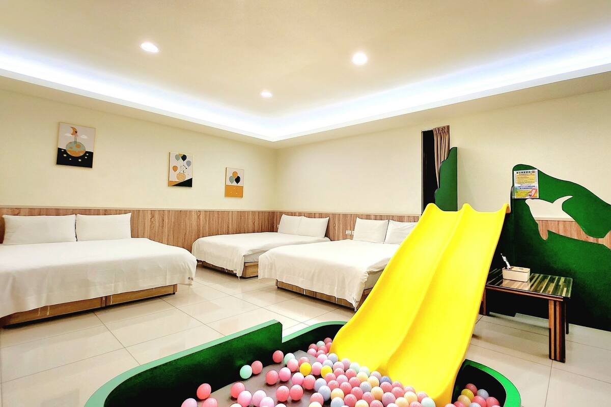 A hotel room with two beds, a yellow slide, and a ball pit.