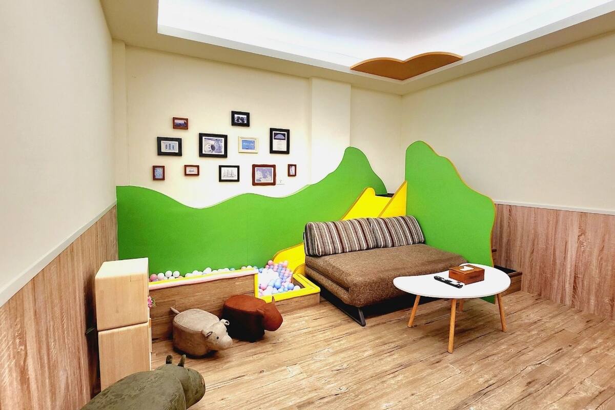 A cozy room with a sofa, a small table, a green wall with framed pictures, and a wooden floor.