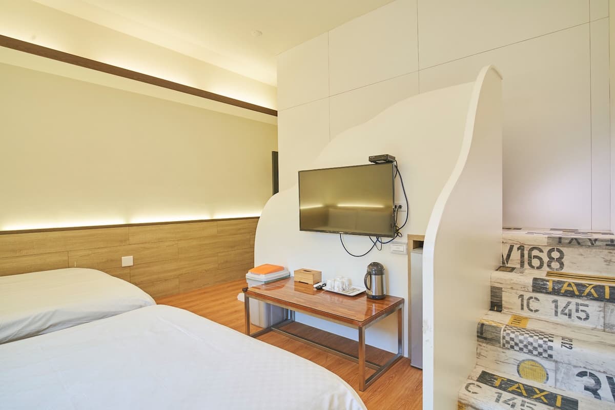 A hotel room with two beds, a wooden desk, a television, and a wall with decorative elements.