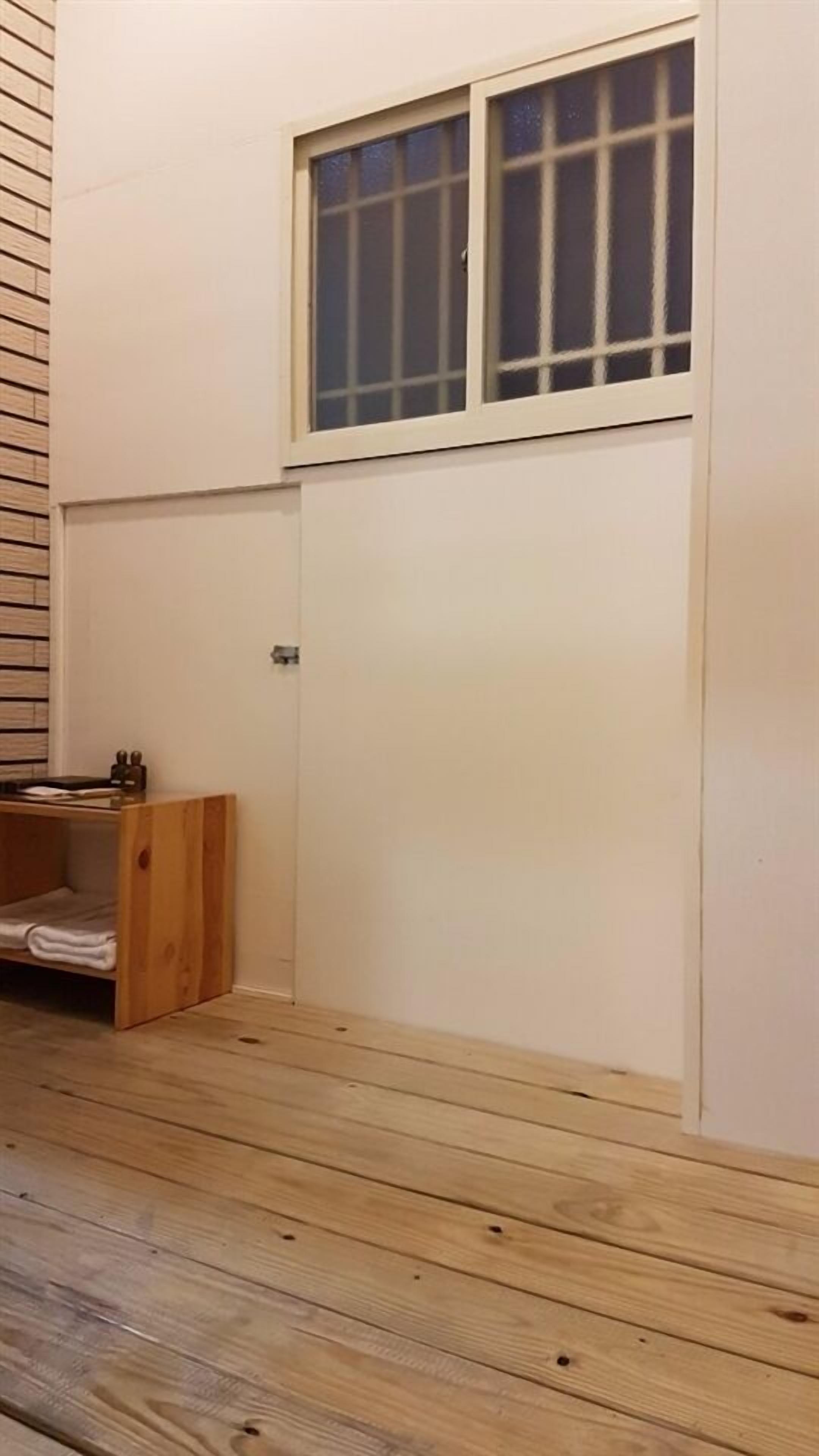 A room with a wooden floor, a window with white frames, and a door with a handle.