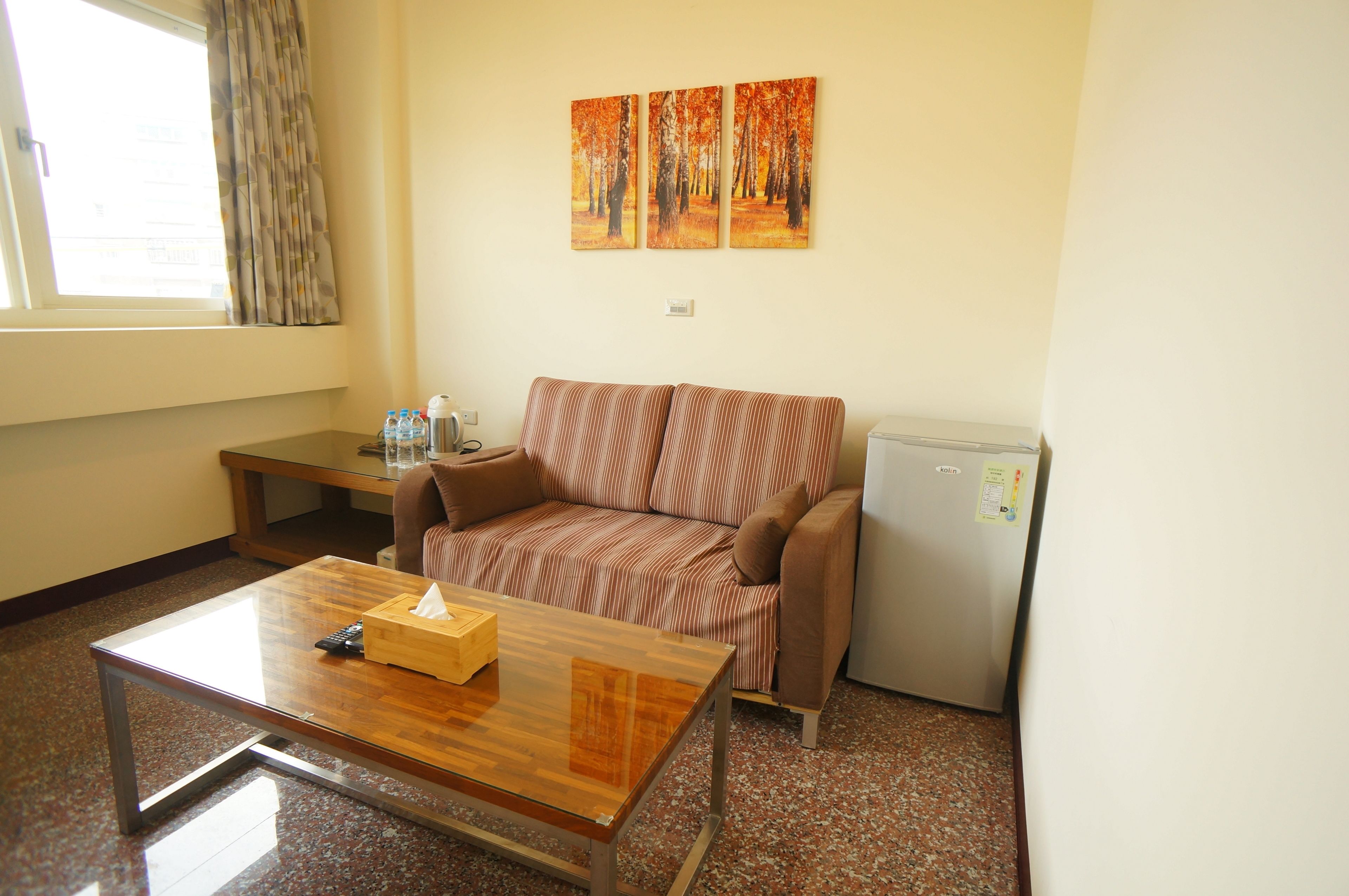 A compact room with a sofa, a small table, a refrigerator, and a window with curtains.