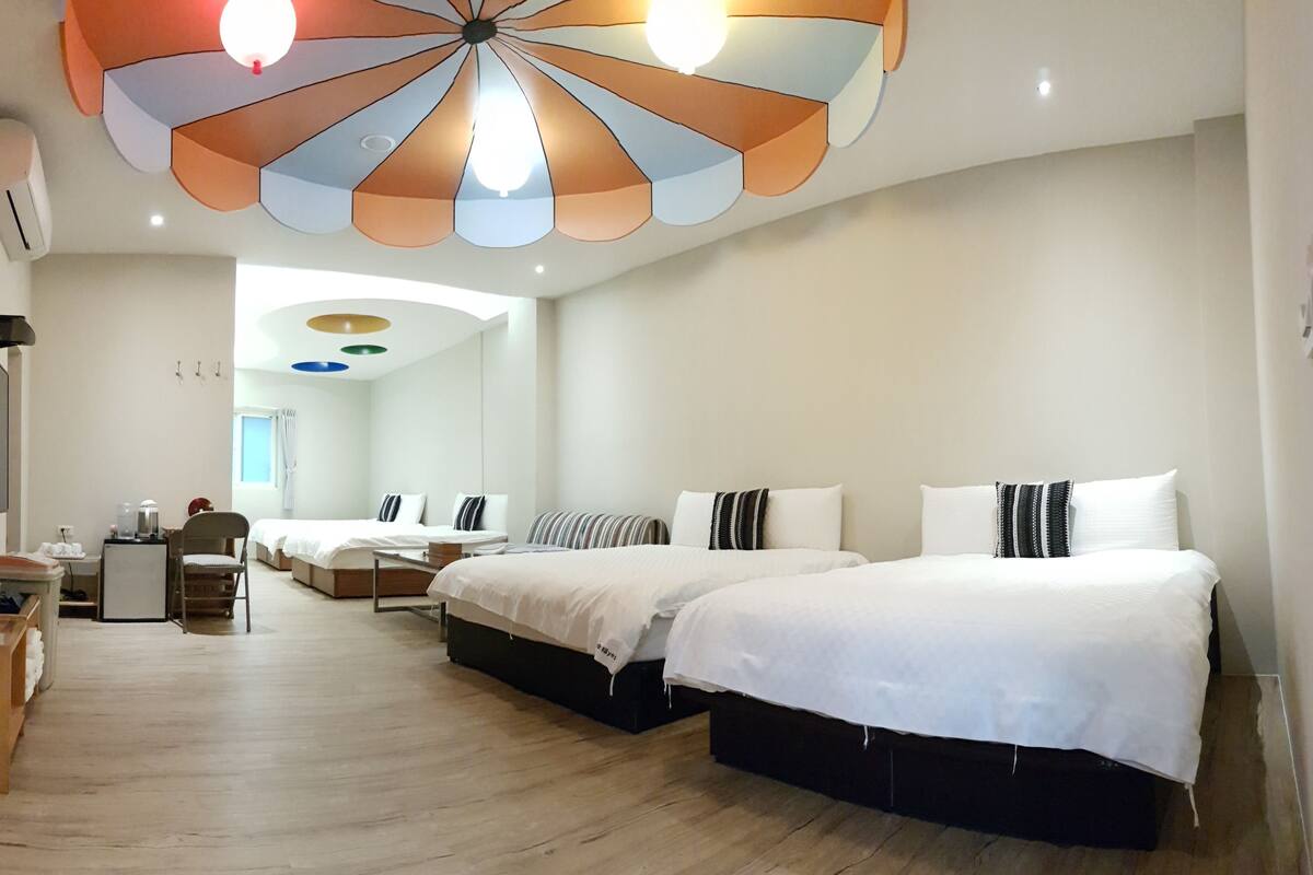 A hotel room with two beds, a wooden bench, a TV, and a ceiling light fixture.