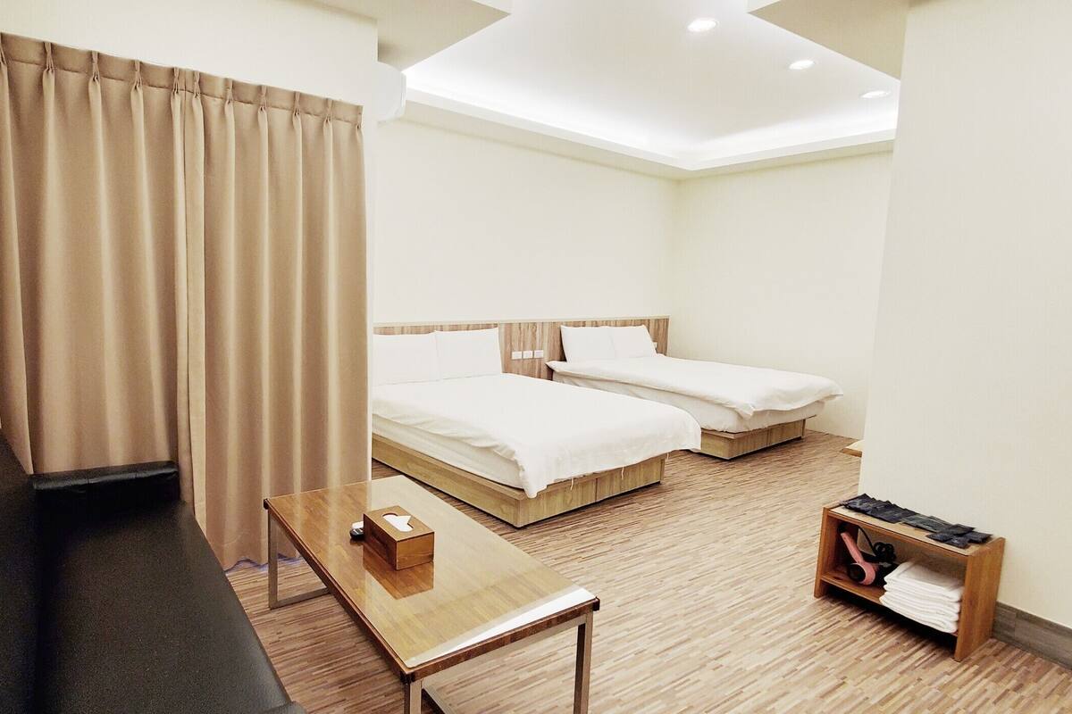 A hotel room with two beds, a desk, a chair, and a small table with a box.