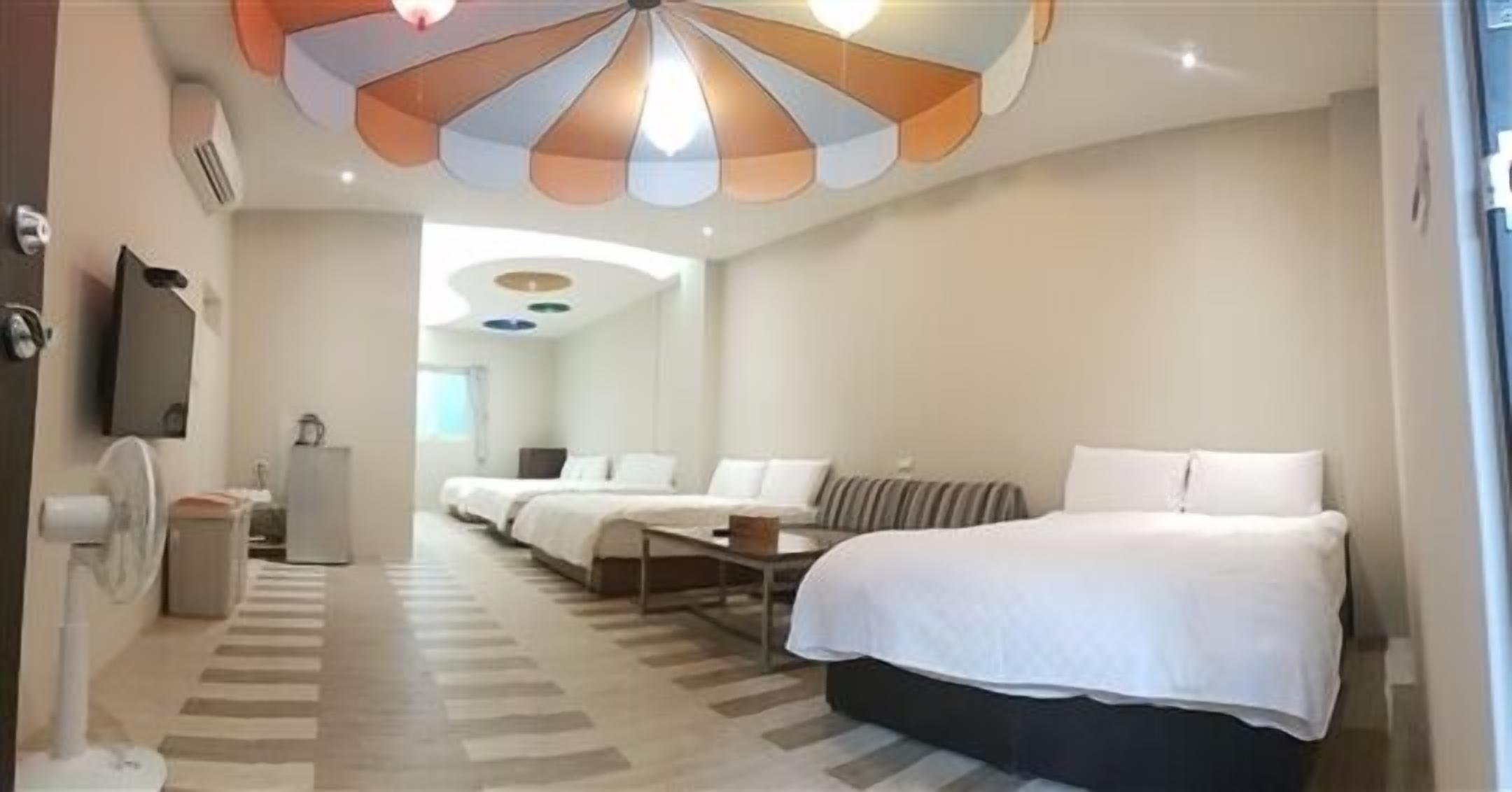 A hotel room with a large bed, a smaller bed, a sofa, a desk, and a ceiling fan.