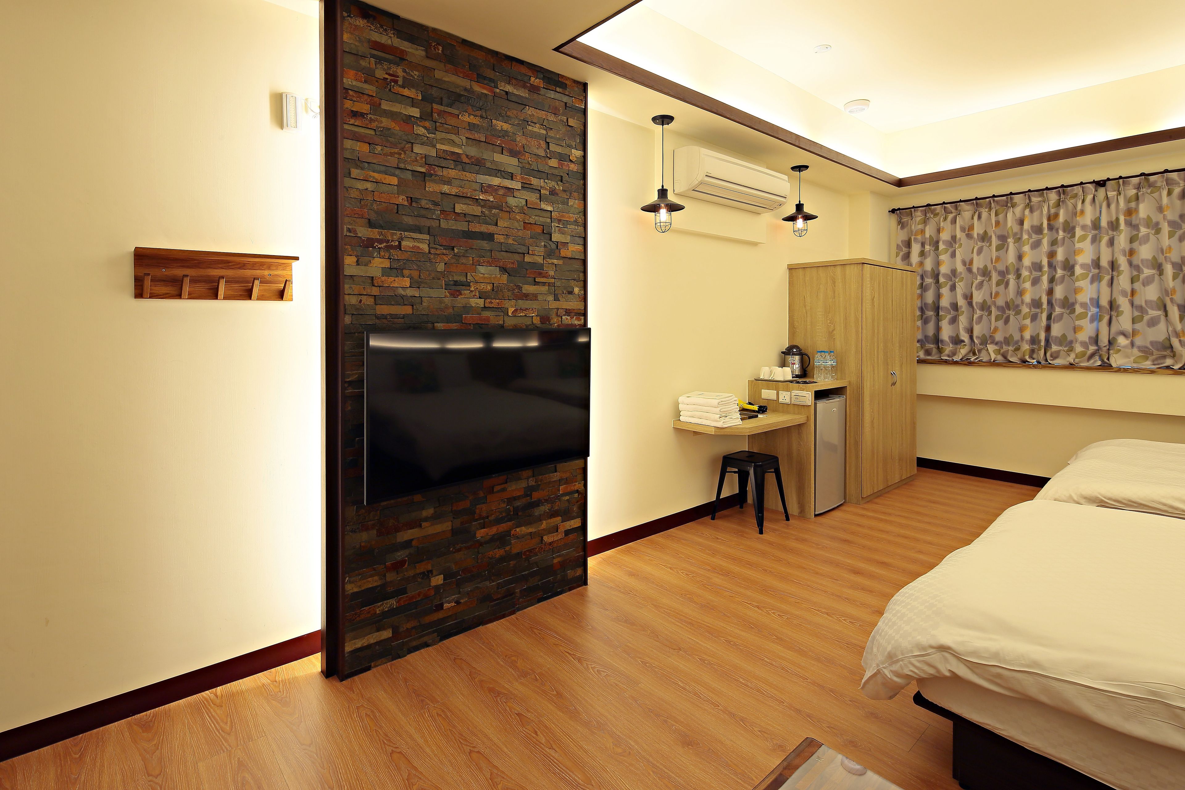 Hotelkamer met houten vloer, een bed, bureau met stoel, kledingkast en een badkamer met douche.