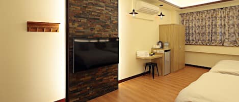 Habitación de hotel con piso de madera, cama, escritorio con silla, armario y baño con ducha.