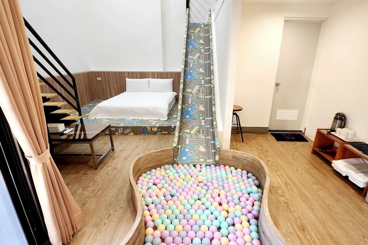 A hotel room with a bed, a wooden floor, a ball pit, and a staircase.