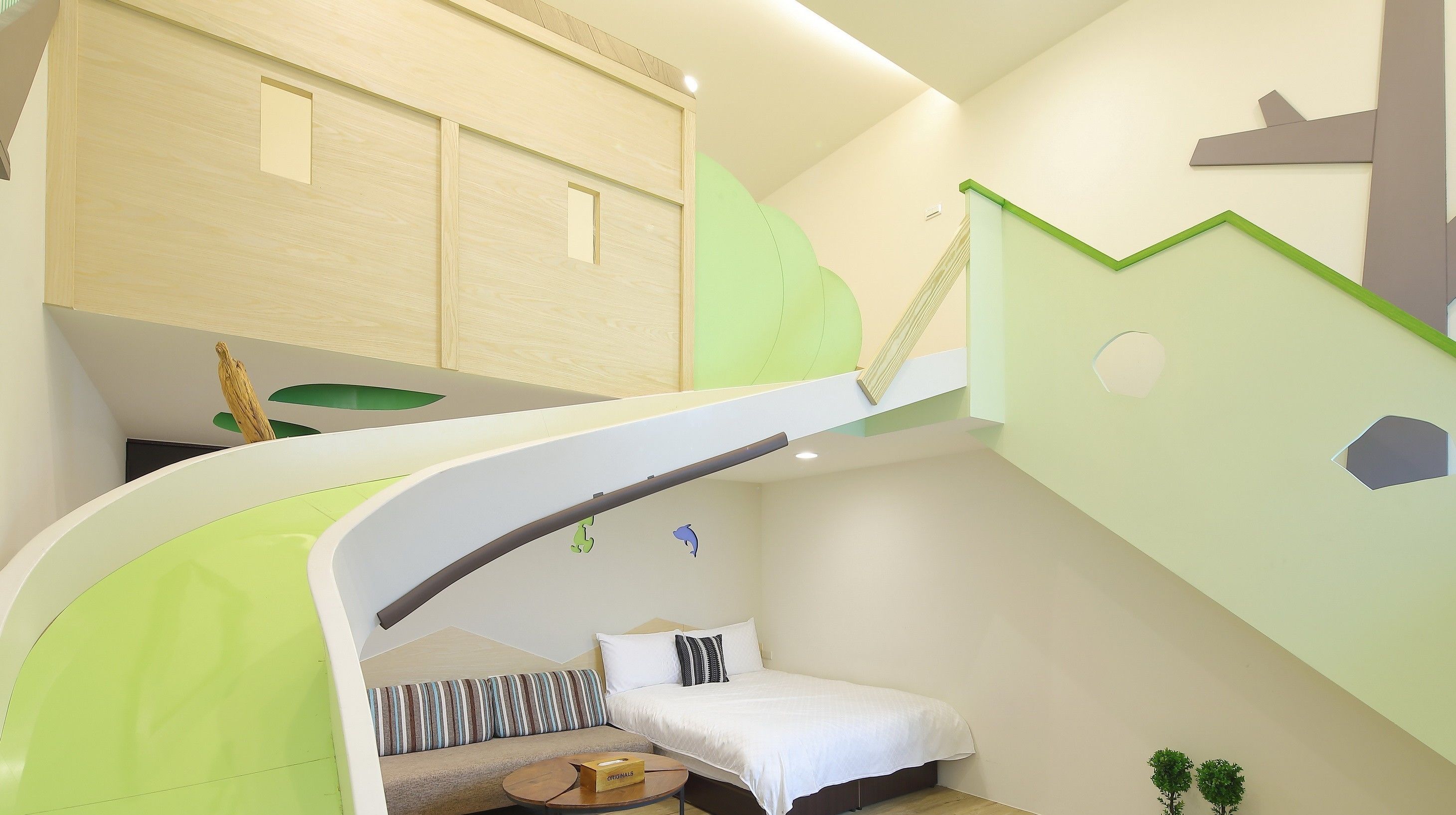 A modern room with a curved staircase, a bed with a striped pillow, and a small table with a box labeled "TICKETS".