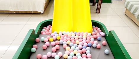 A play area with a yellow slide and a ball pit filled with multicolored balls.
