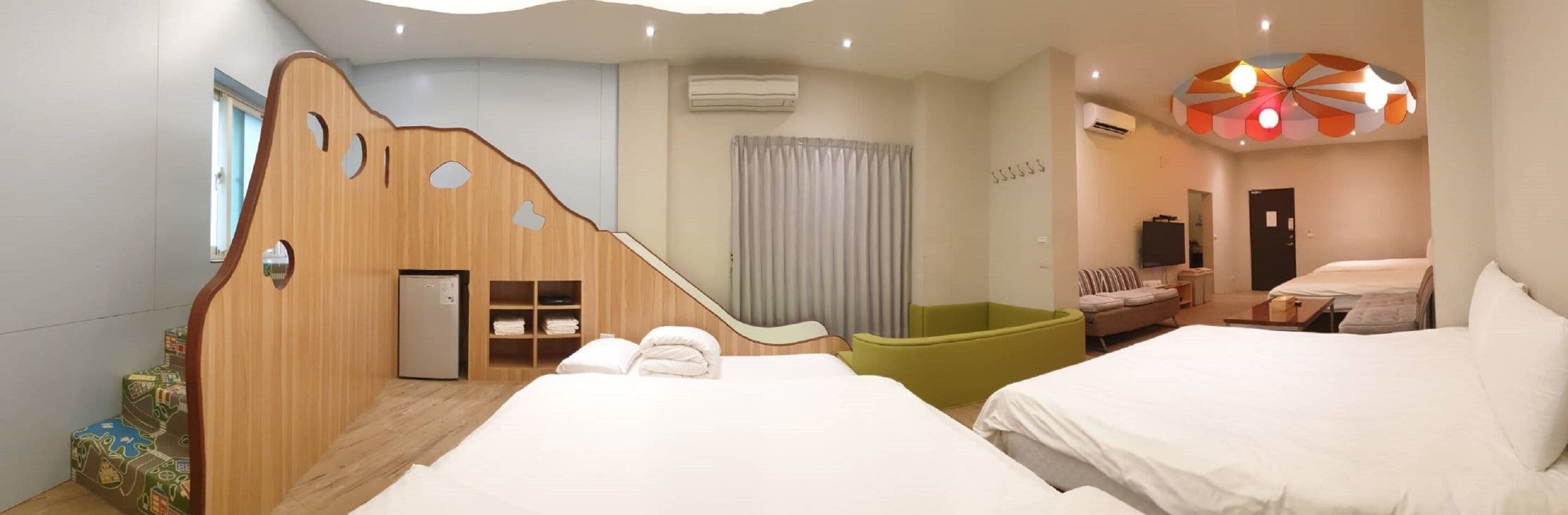 Ein Hotelzimmer mit zwei Betten, einer Holzwand, einem grünen Sessel, einem kleinen Tisch und einer Deckenleuchte.