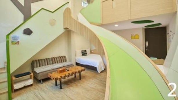 A room with a bed, a sofa, a small table, and a wooden floor. There is a green wall with a tree design and a door in the background. - Happiness Yes Inn (Luodong)