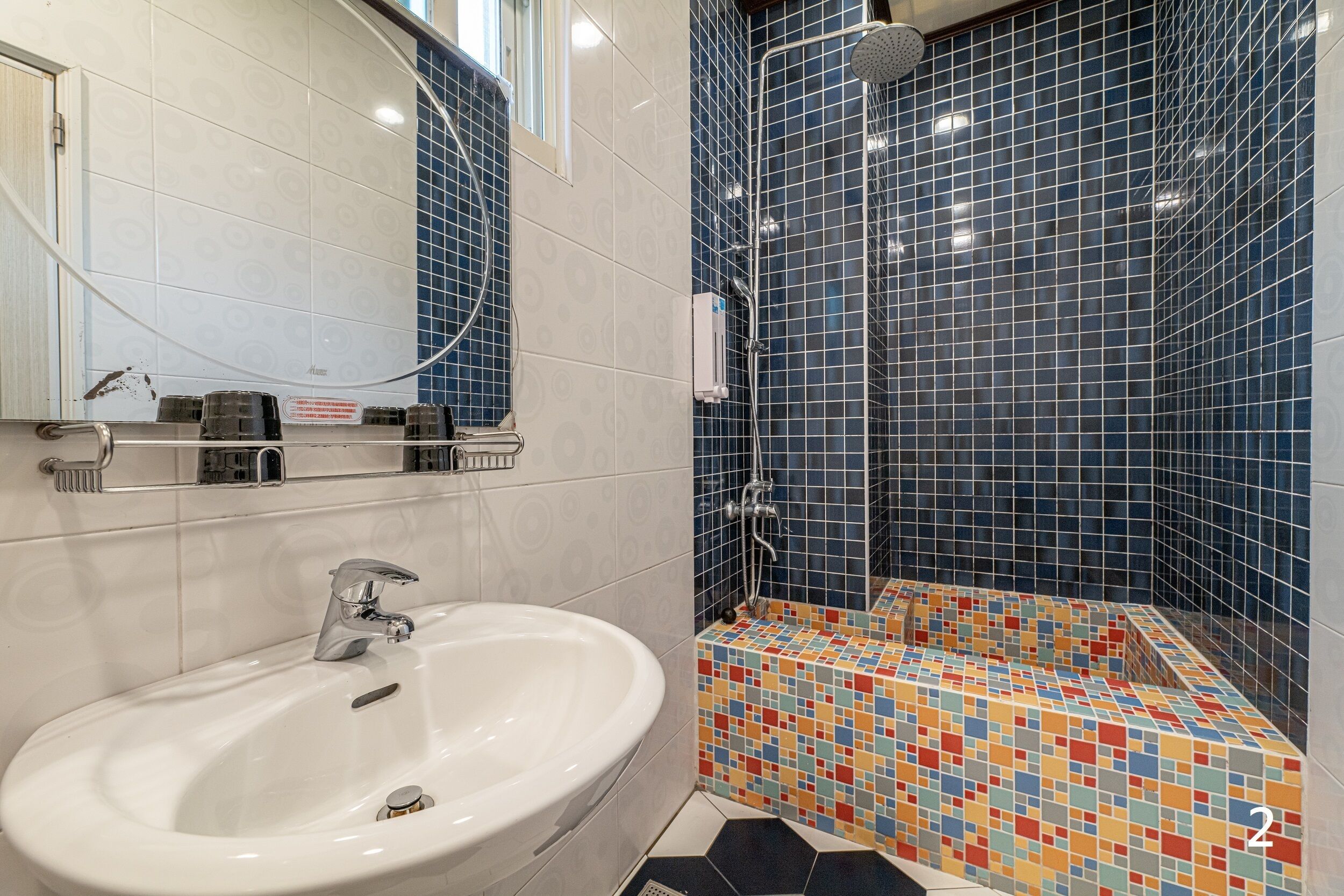 A bathroom with a white sink, a shower with blue tiles, and a colorful mosaic floor.
