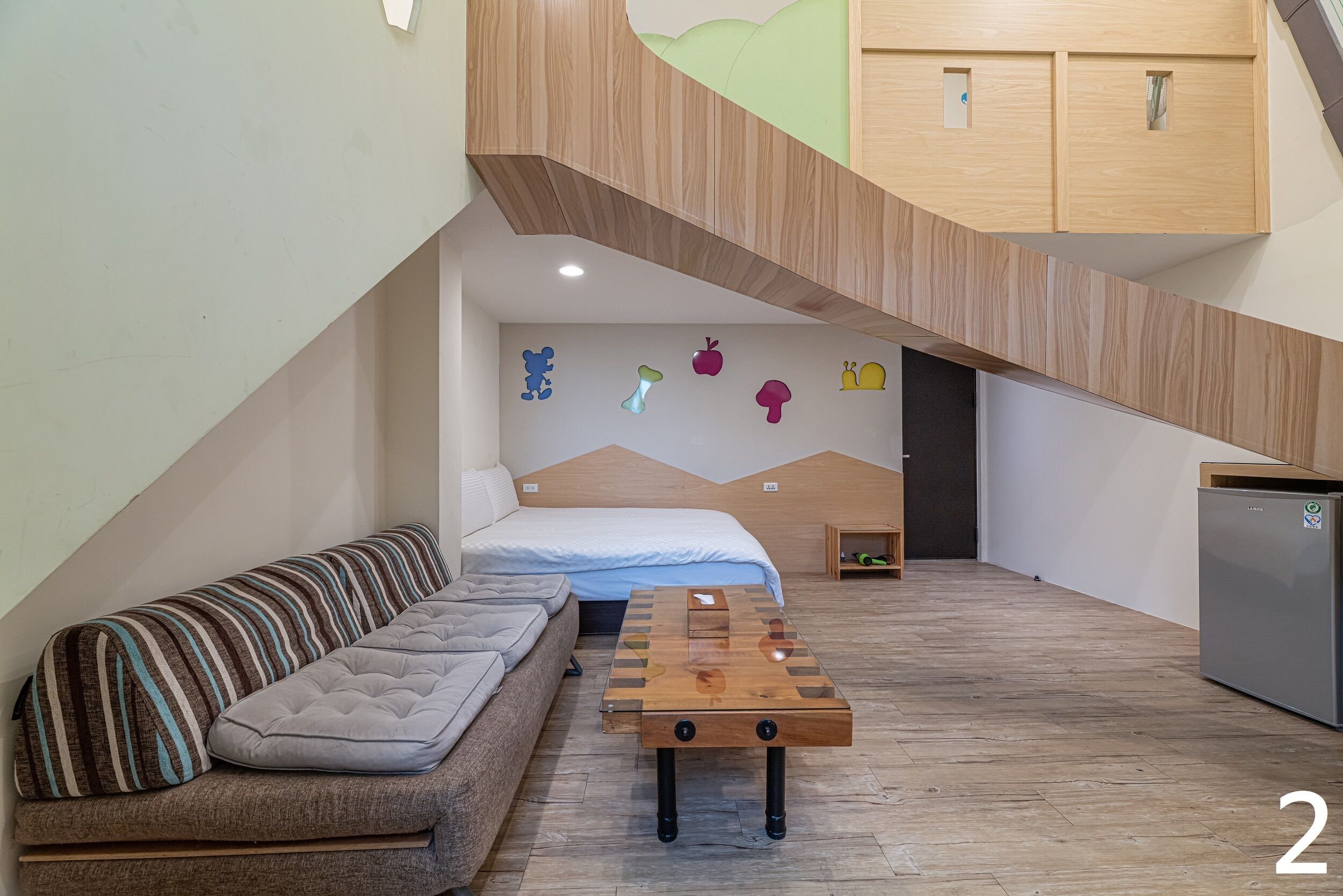 A loft-style bedroom with a loft bed, a sofa, a wooden coffee table, and a kitchenette.
