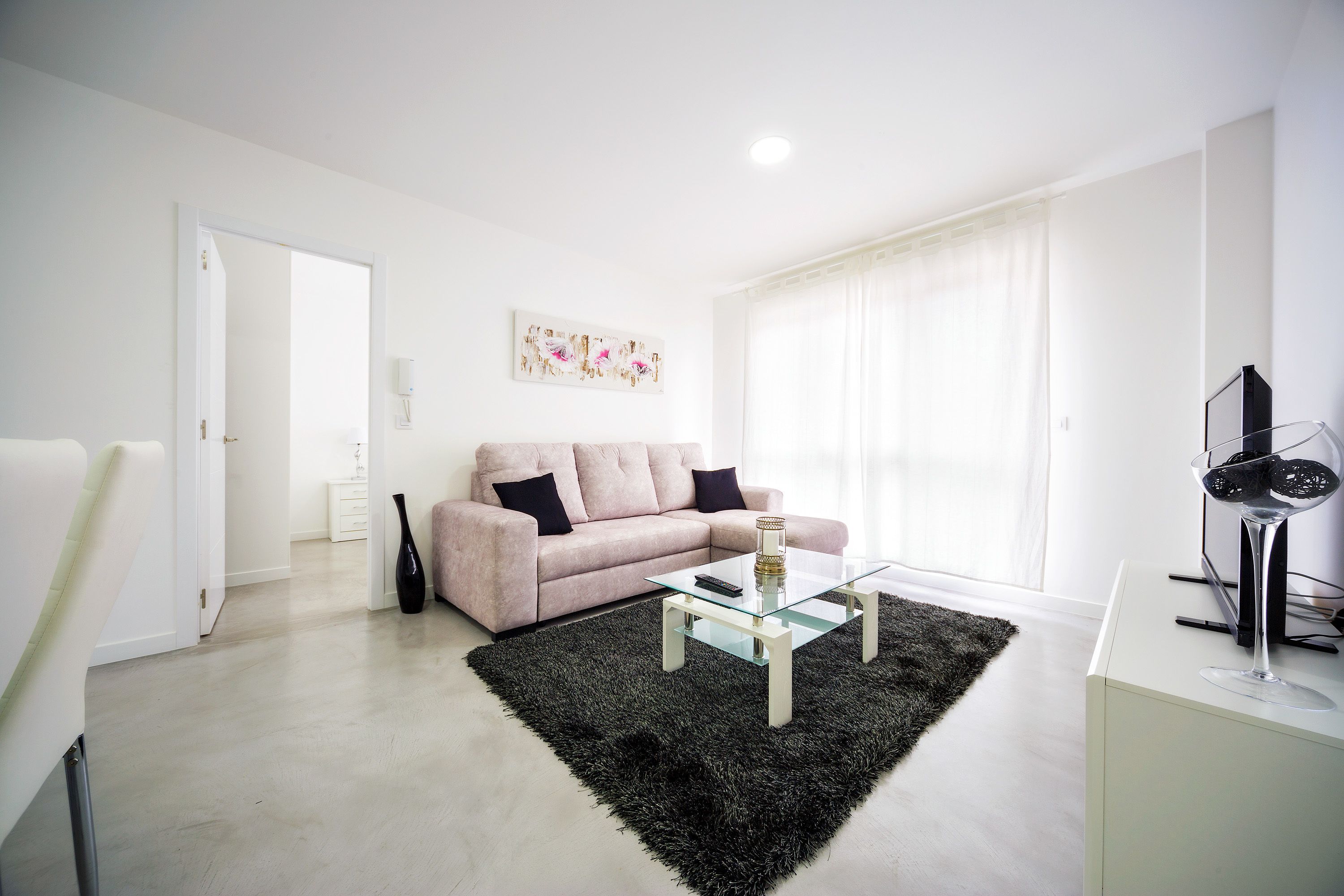 Uma sala de estar moderna com um sofá, uma mesa de centro de vidro e um tapete preto.