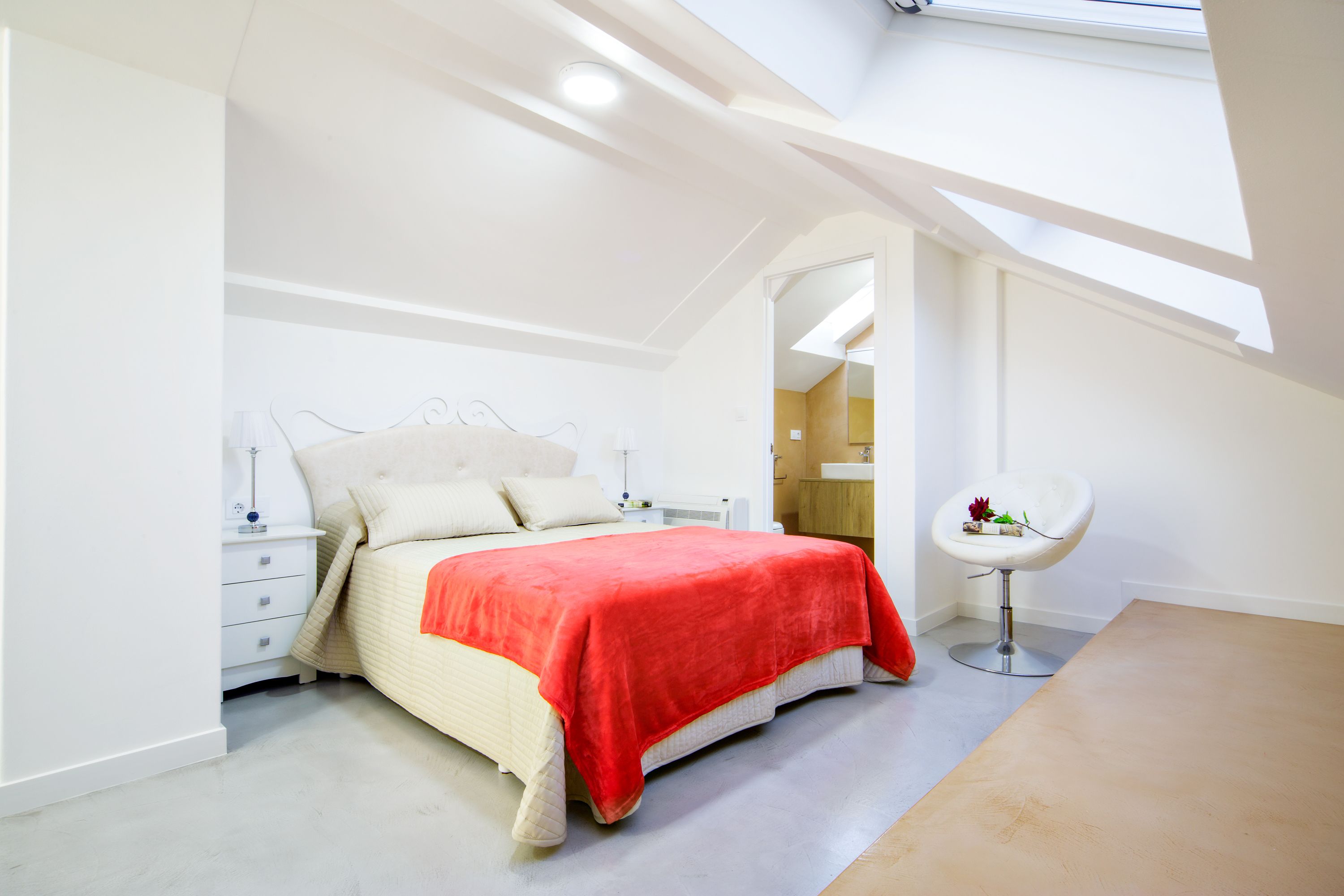 Un dormitorio moderno con una cama, mesitas de noche, una silla y un tragaluz.